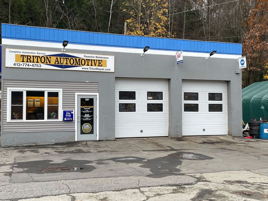 Auto repair shop exterior with gray facade, blue roof trim, and two white garage doors.