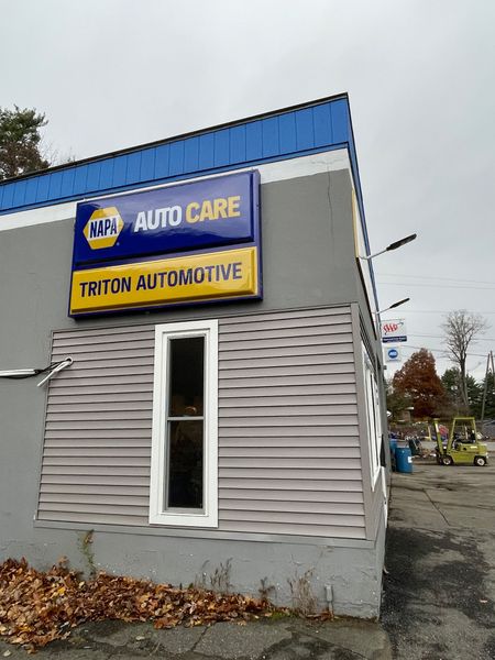 Auto care shop exterior with blue-and-yellow sign, gray siding, and a narrow window.