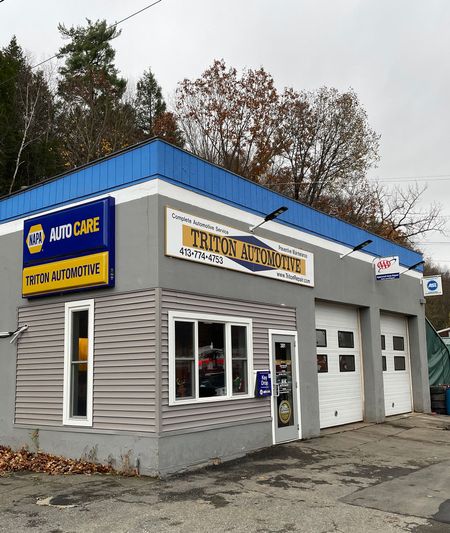 NAPA Auto Care auto body shop with blue trim, gray siding, and garage doors on an overcast day