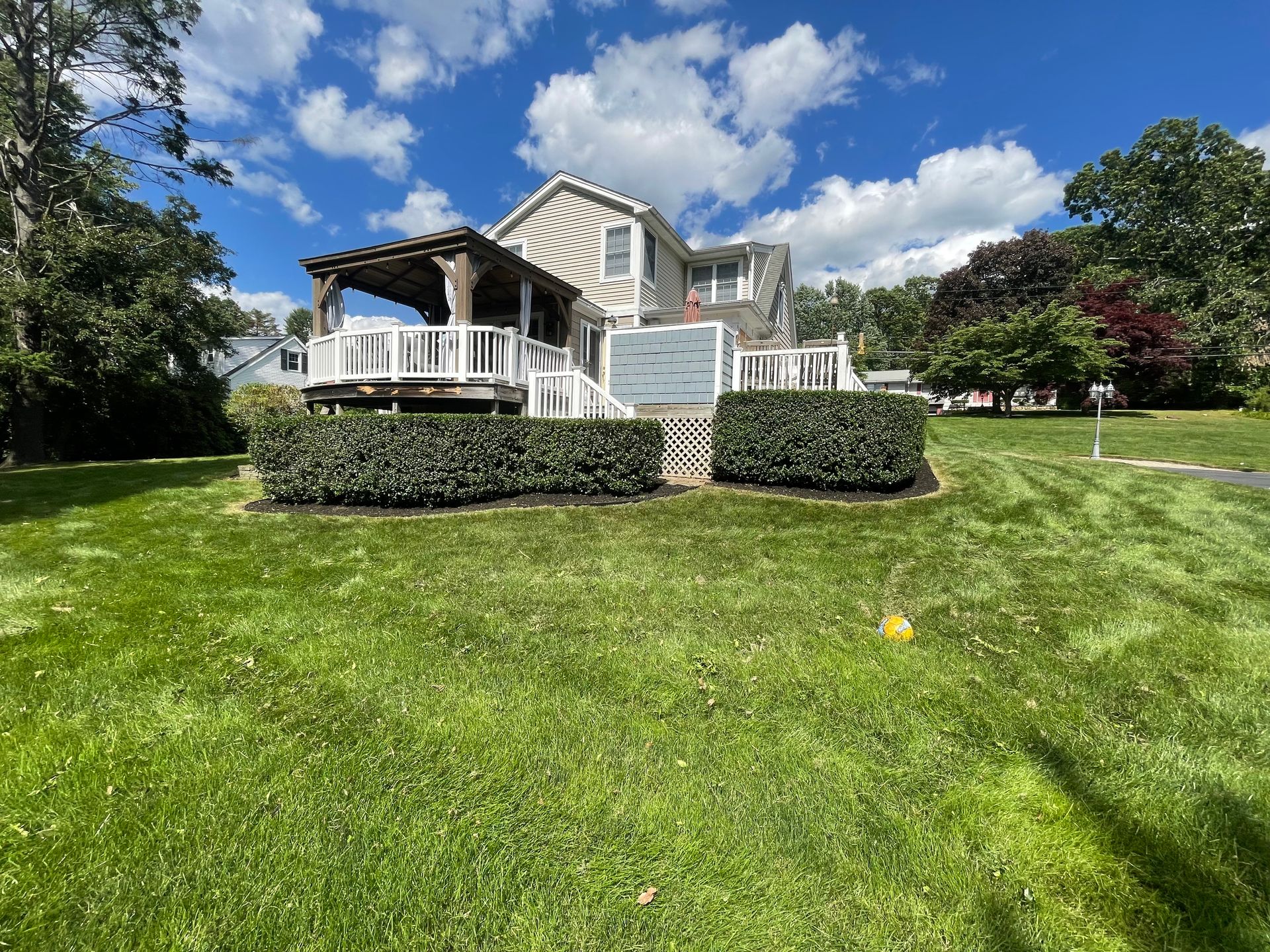 House with a deck, pergola, and manicured lawn under a cloudy blue sky.