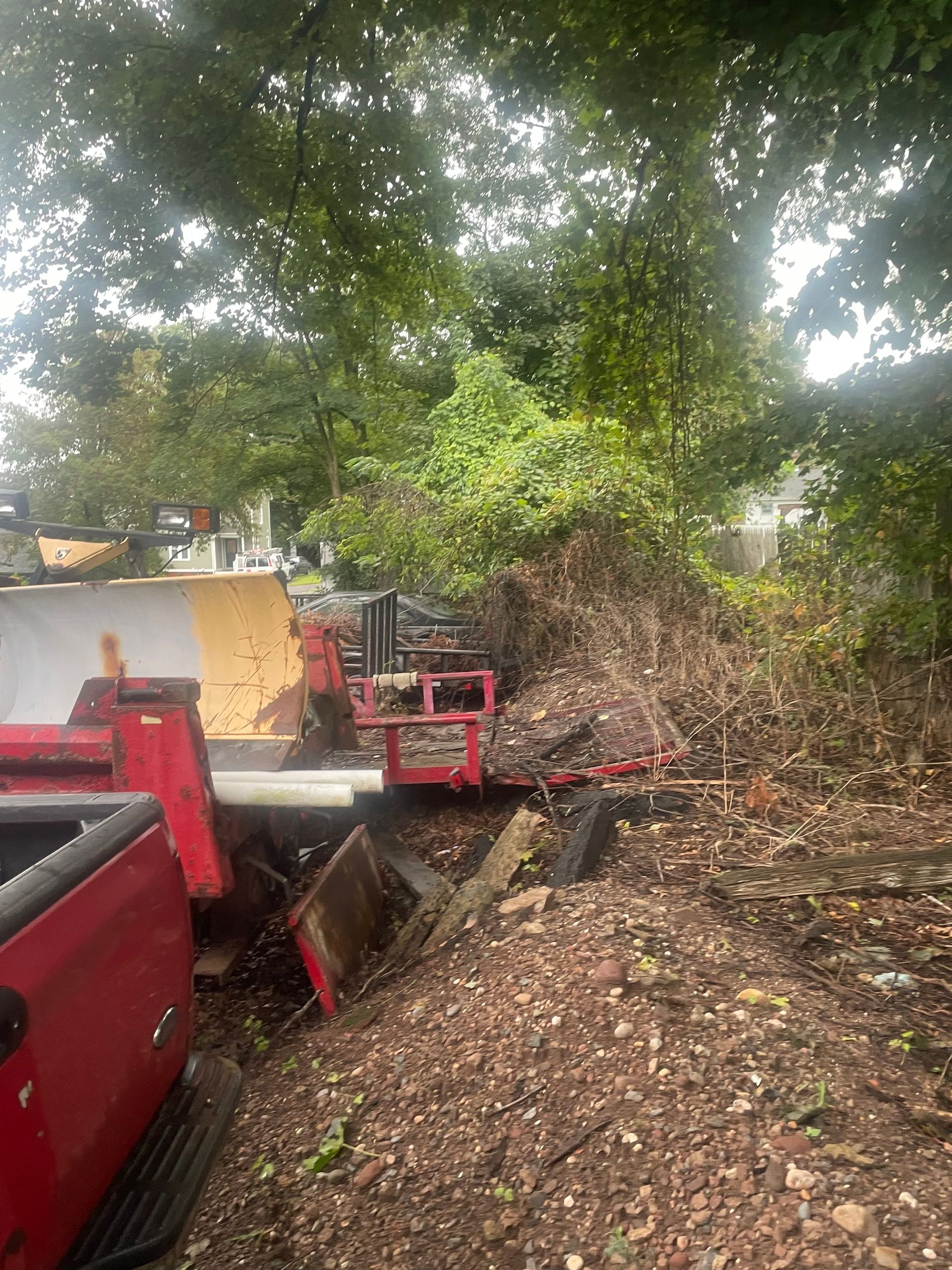 Red truck next to a pile of debris and trees. Overcast day.