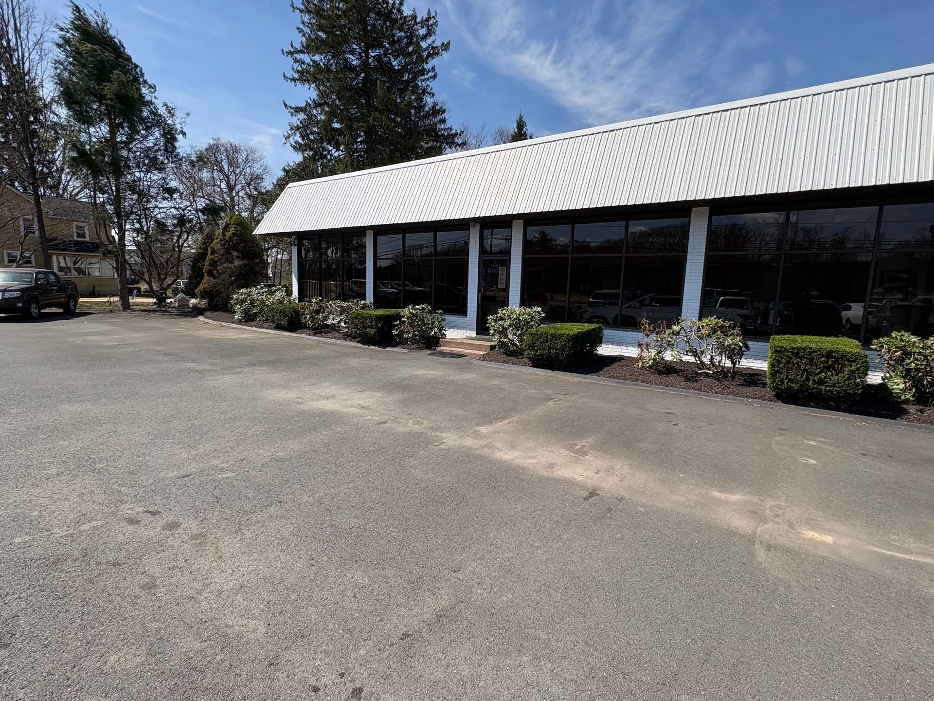 Exterior view of a commercial building with large windows, a white roof, and bushes along the foundation.