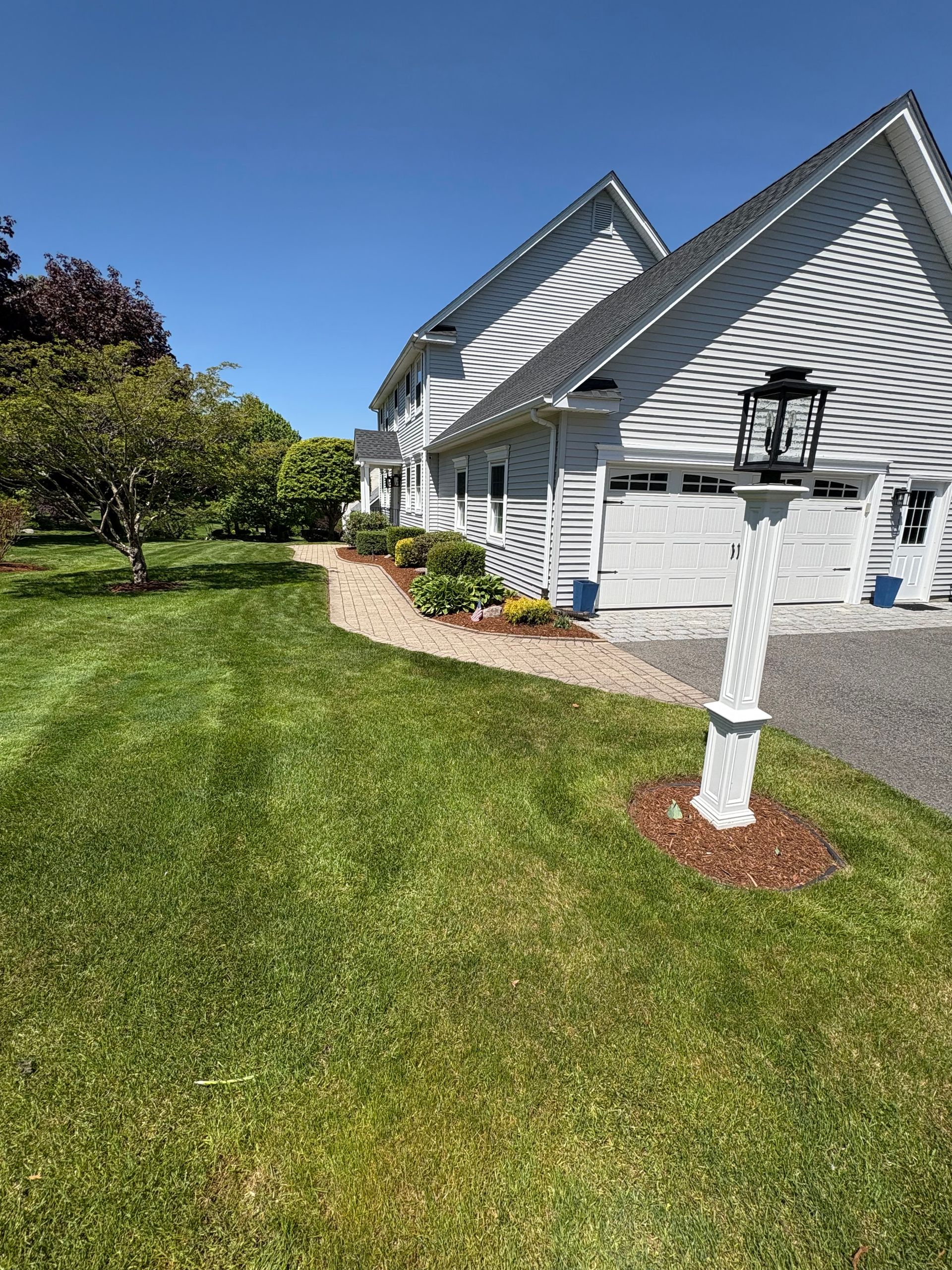 Side view of a two-story white house with a paved pathway, lawn, and blue sky.