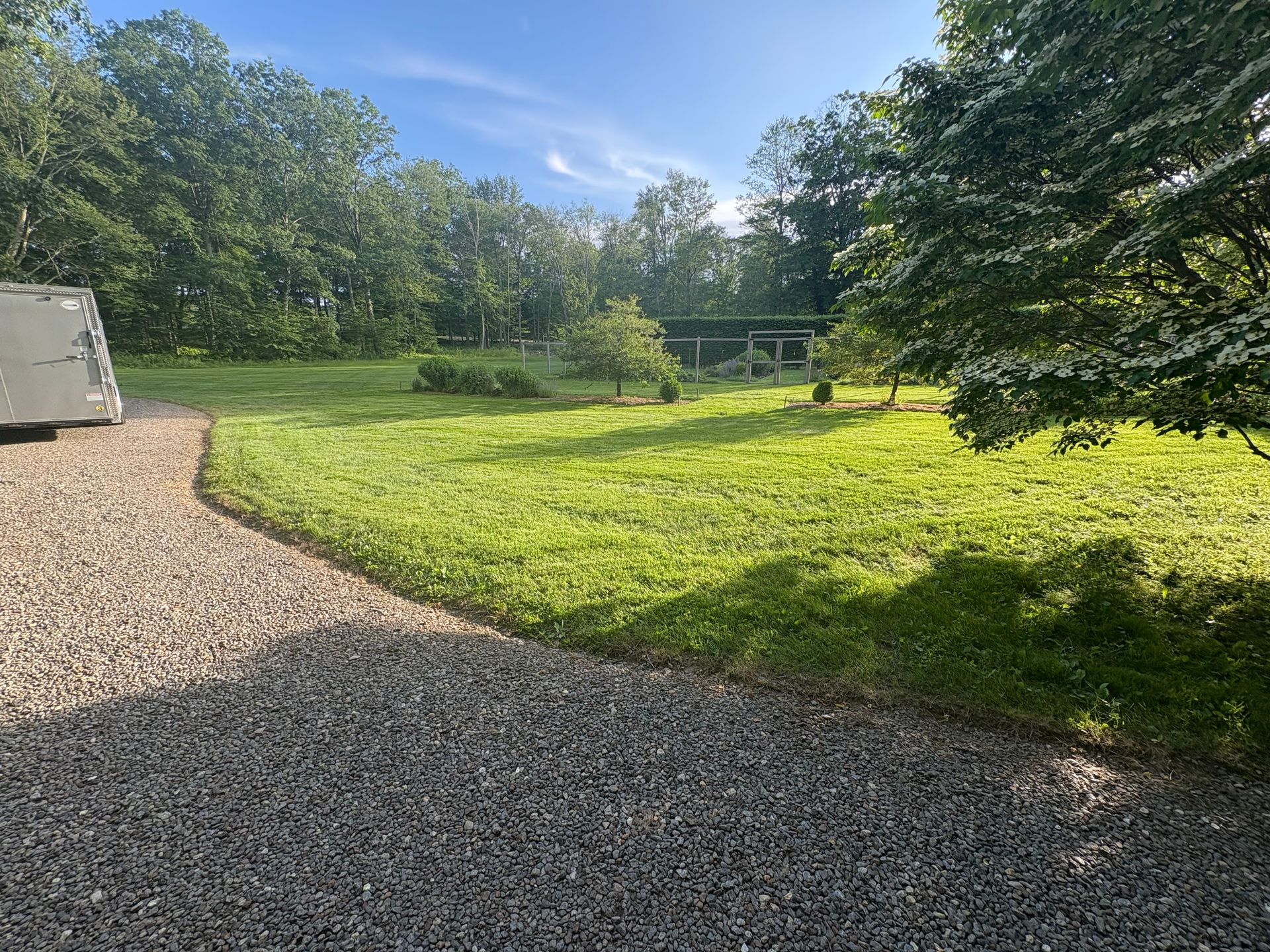 Gravel path leads to a grassy yard with trees, under a blue sky.