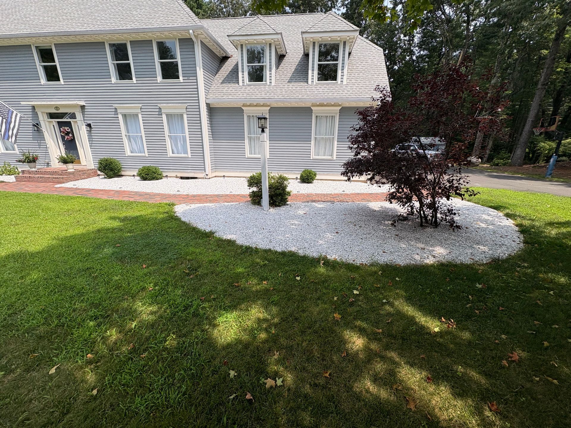 Gray house with white stone landscaping, a dark red tree, and green grass.