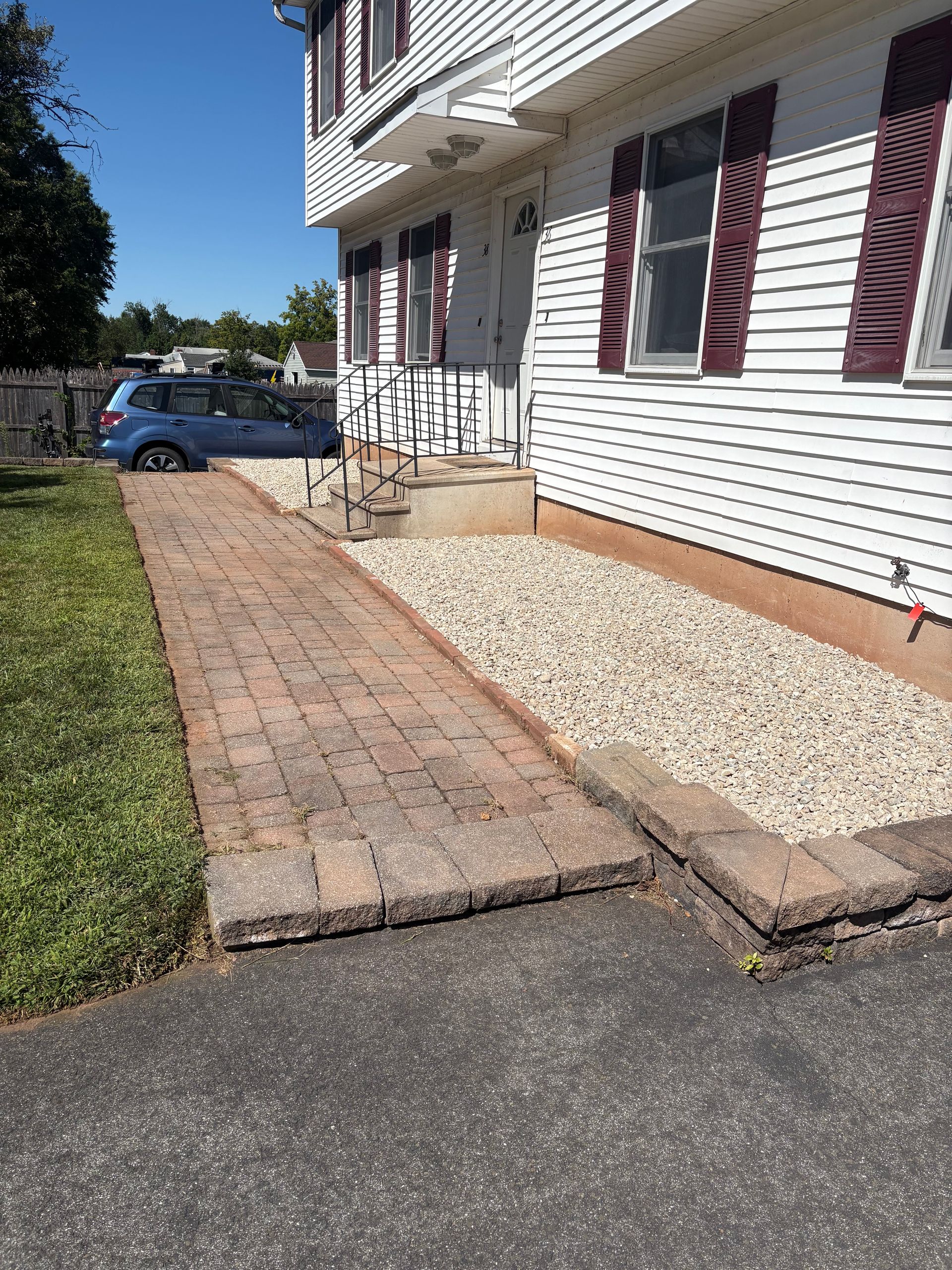Brick pathway and gravel bed next to a white house with burgundy shutters.