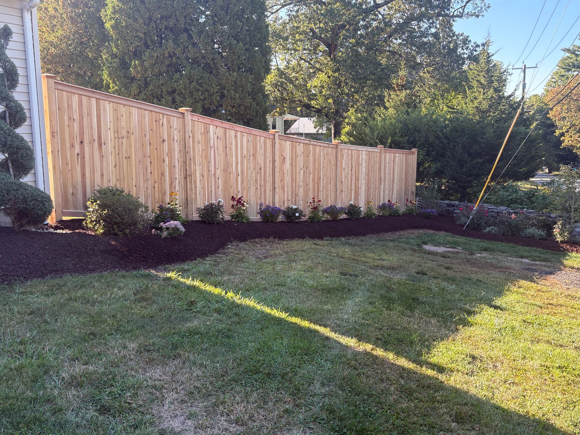 Wooden fence bordering a landscaped yard with green grass and dark mulch.