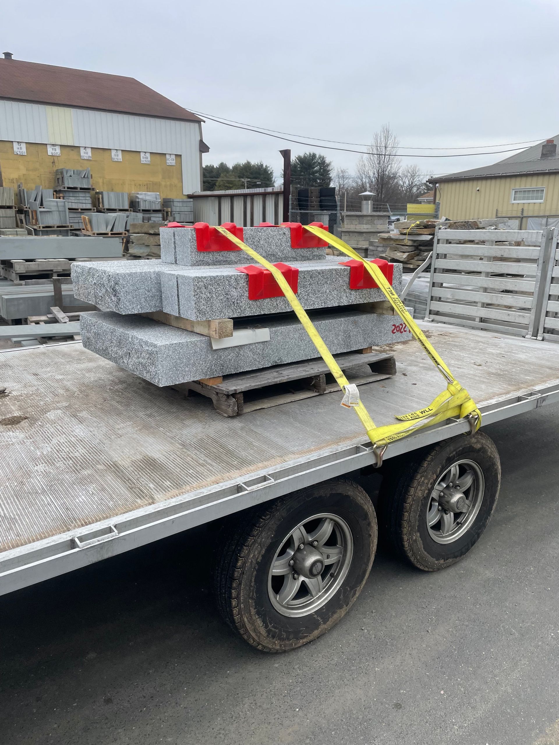 A stack of gray stone slabs secured with yellow straps on a trailer.