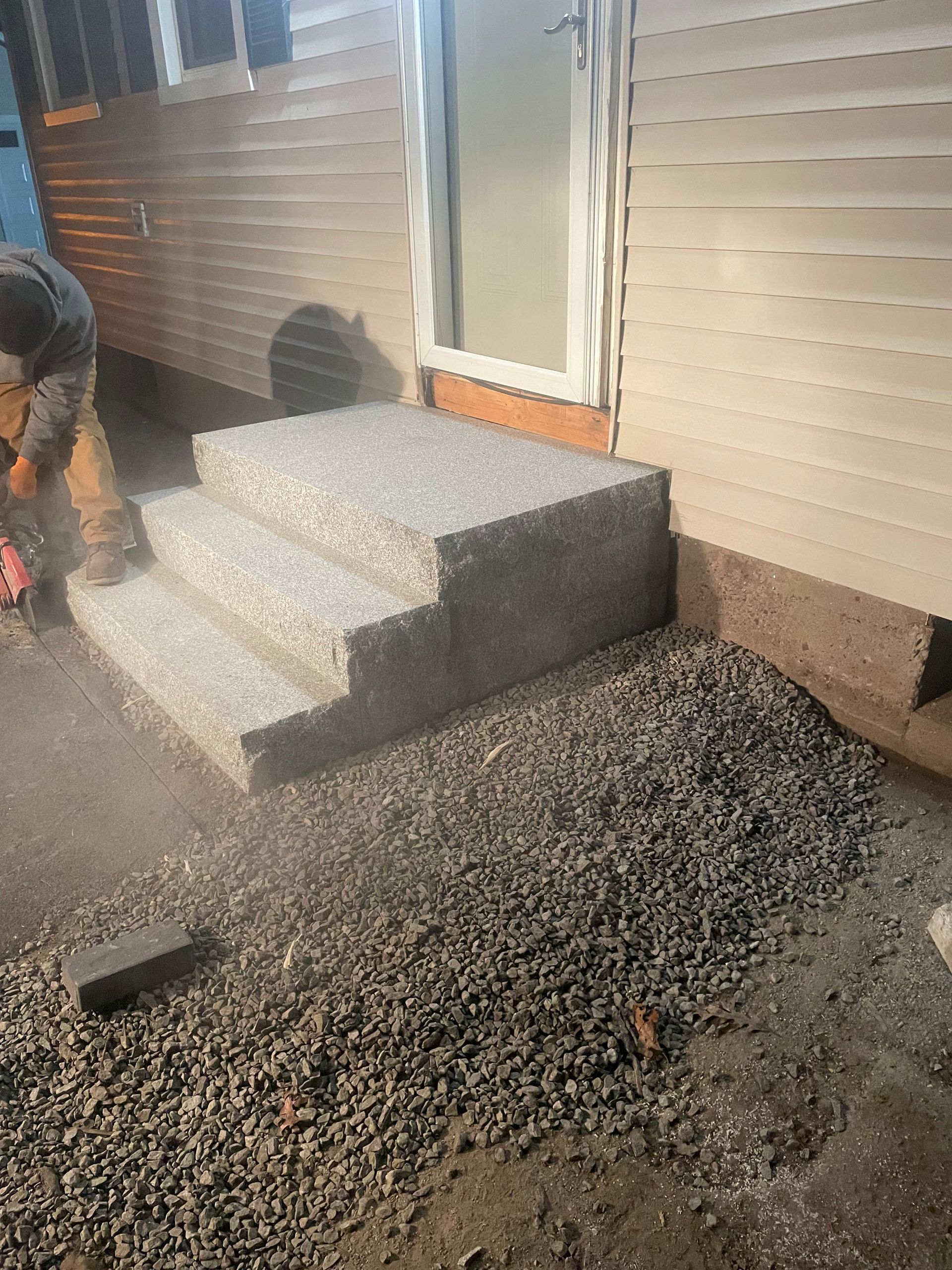 Steps leading up to a door, made of speckled gray stone. A person is working nearby.