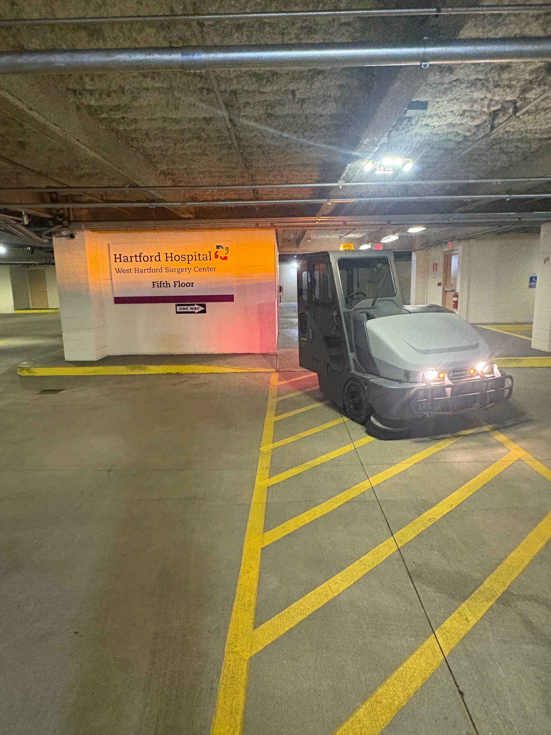 Car in an underground parking garage beside a yellow-striped loading zone and wall sign.
