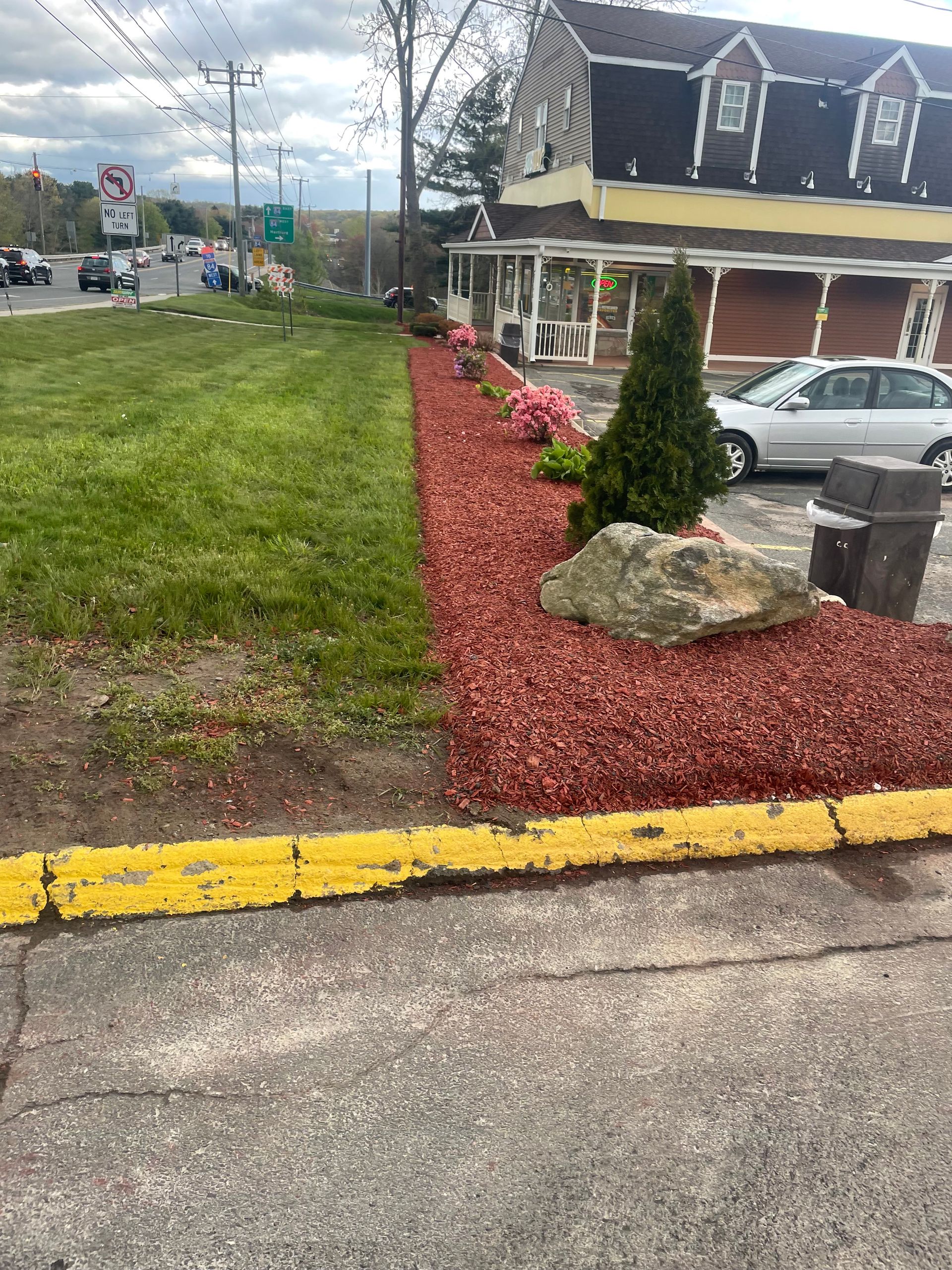 Red mulch and flowerbed by yellow curb, a building, grass, and a car.