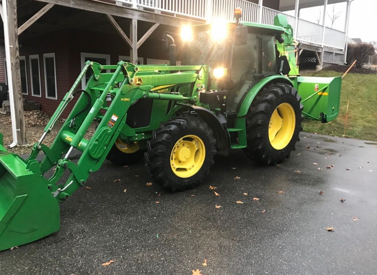 Green John Deere tractor with snowblower and front loader on driveway.