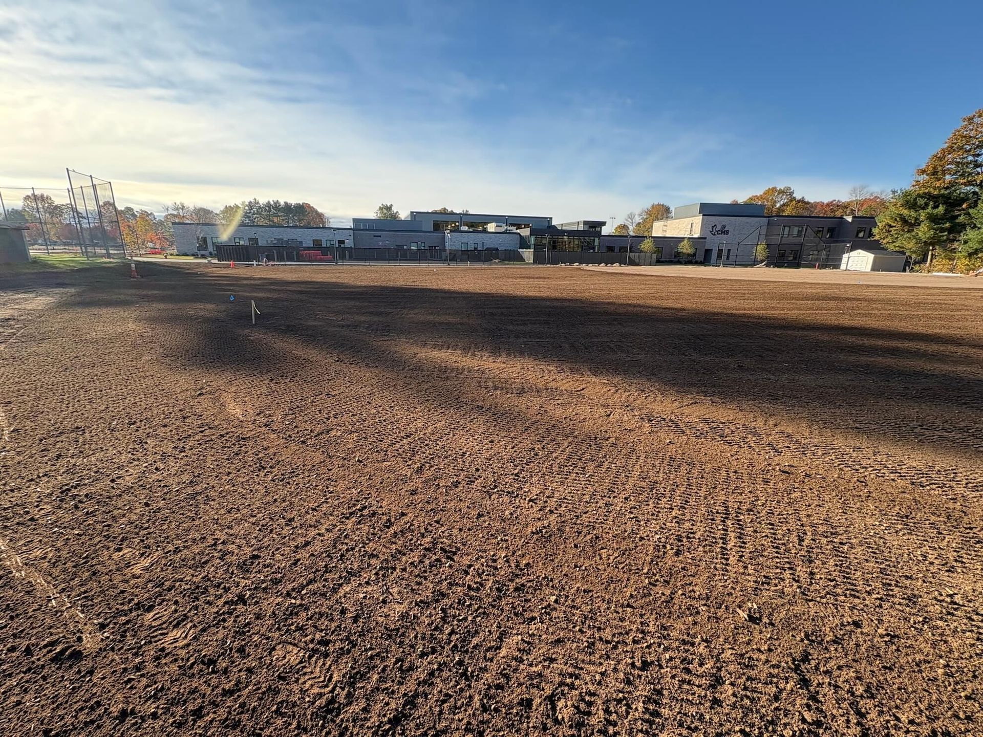 Plowed brown field under a clear blue sky, with houses and trees along the horizon.