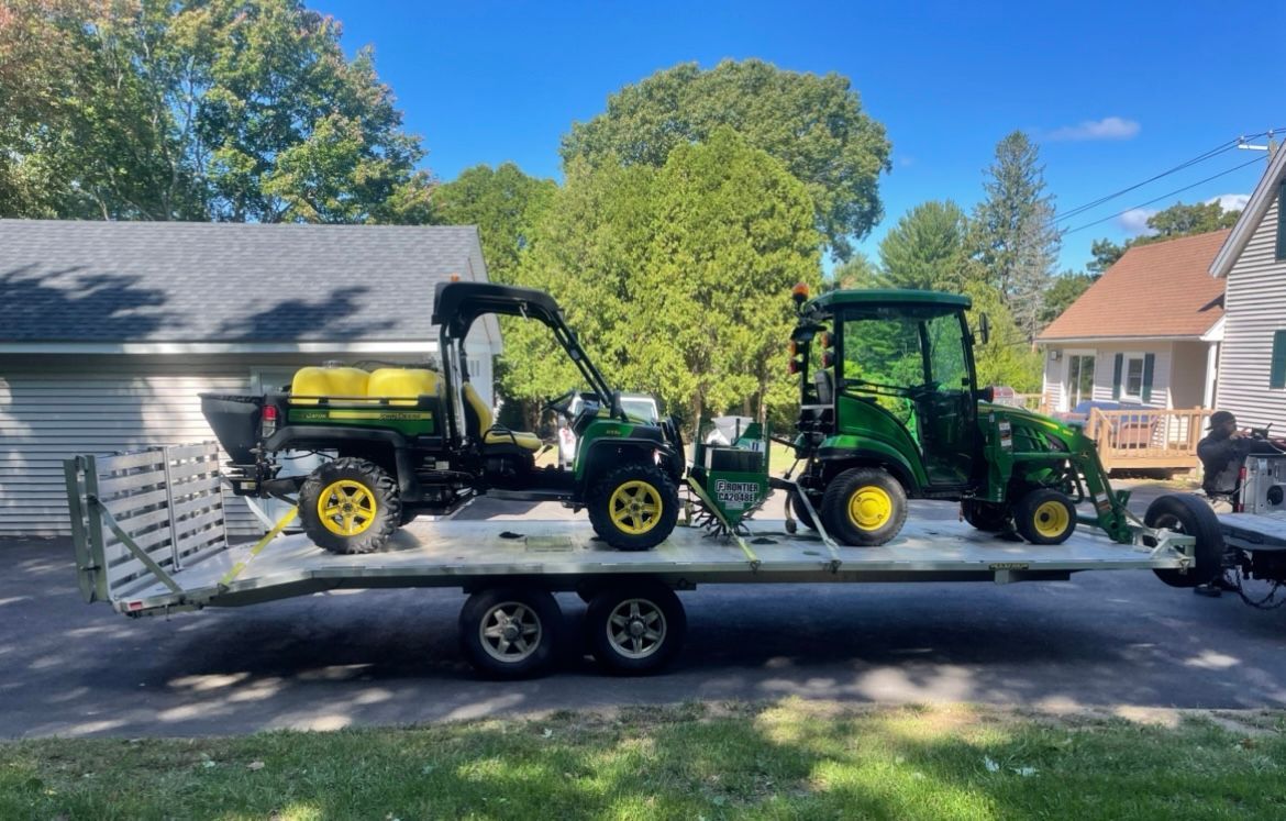 Two John Deere utility vehicles on a trailer in a suburban driveway