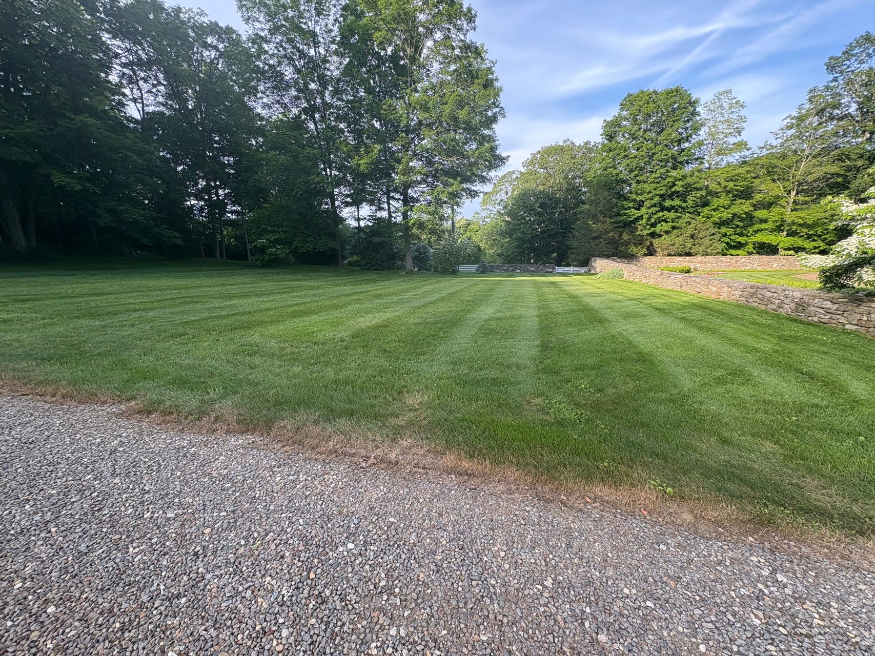 Gravel path beside a mowed grassy lawn bordered by trees under a bright blue sky