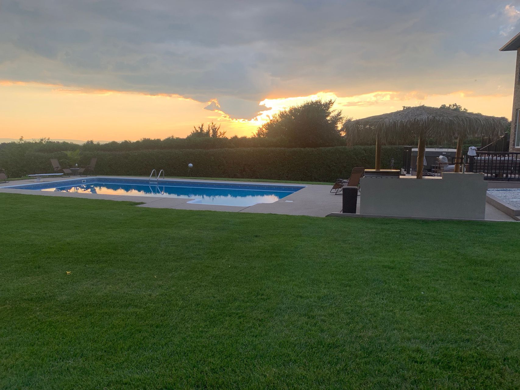Grassy park at sunset with a covered pool, trees, and a walkway railing.