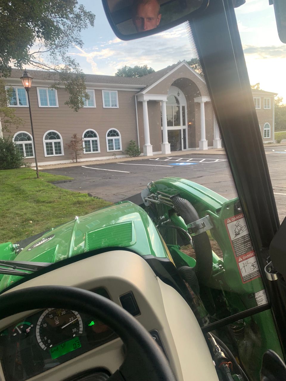 View from a tractor cab toward a brick building with white columns and arched windows