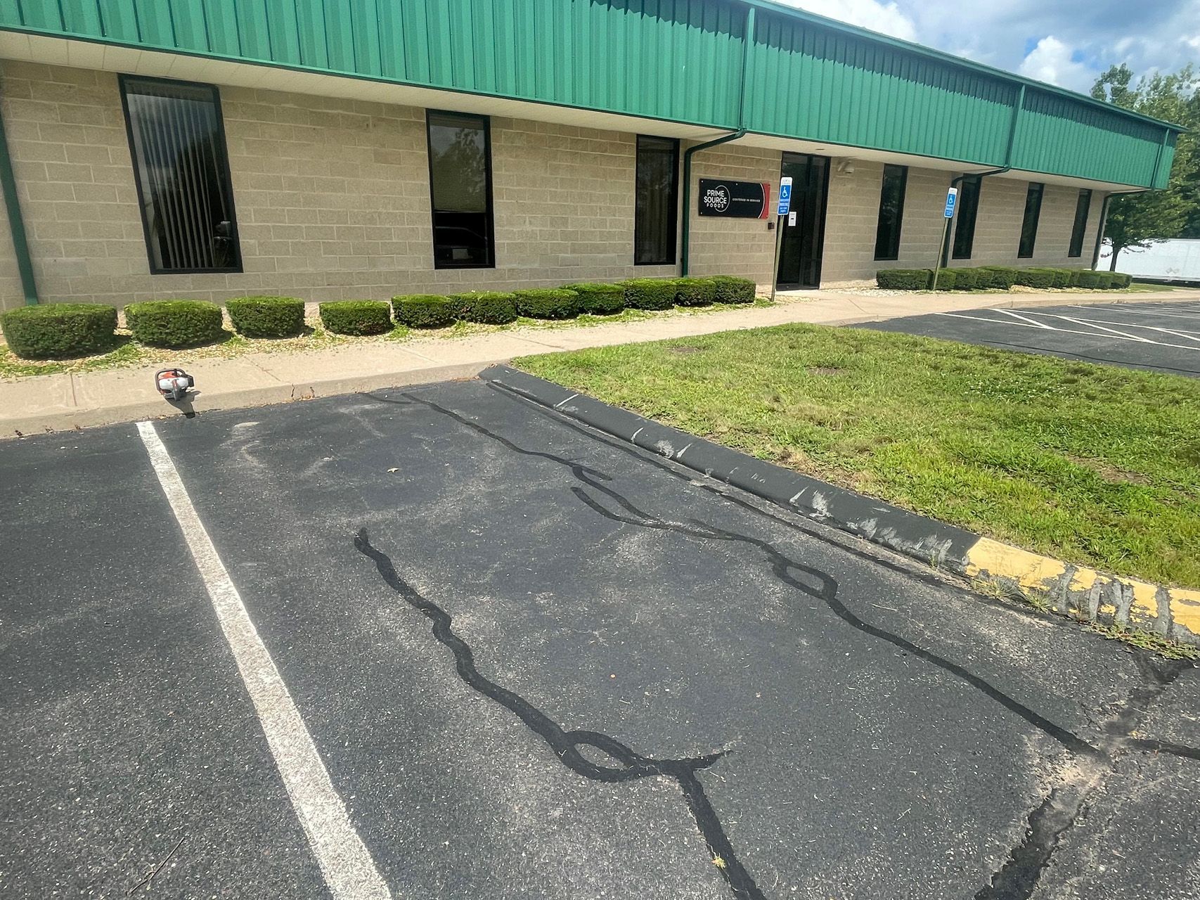 Commercial building with green roof, cracked asphalt parking lot, and sidewalk entrance.