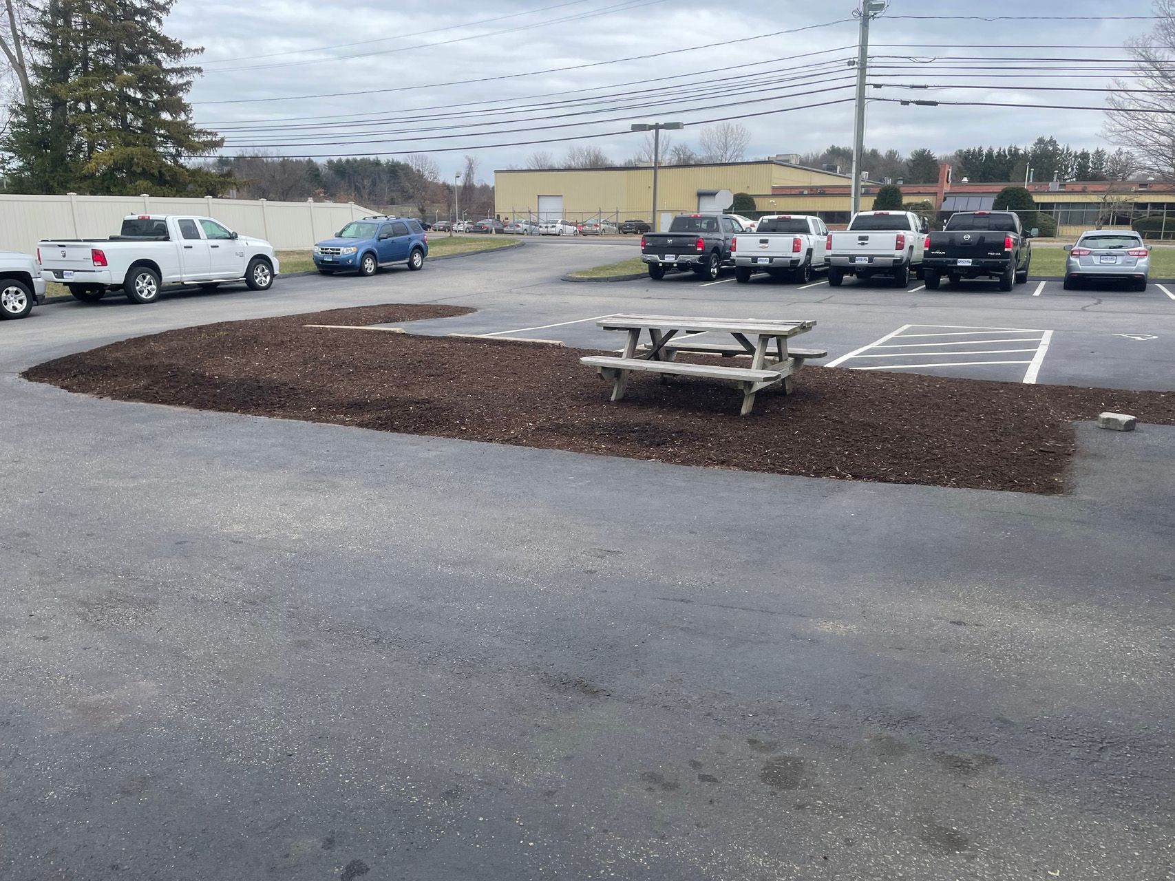 Parking lot with a picnic table on a mulch island under a cloudy sky