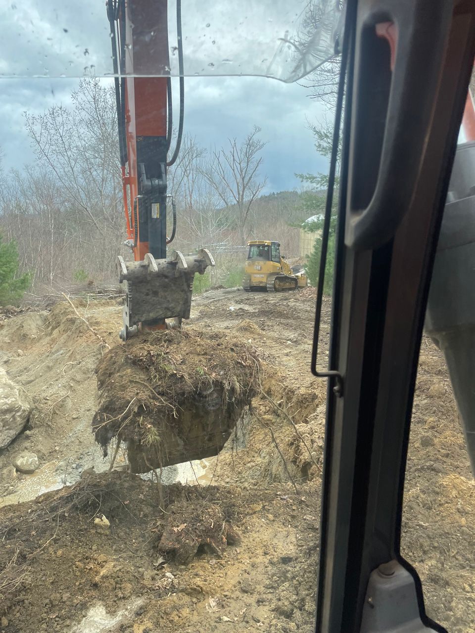 Excavator lifting a large root ball in a muddy construction site with a bulldozer in the background
