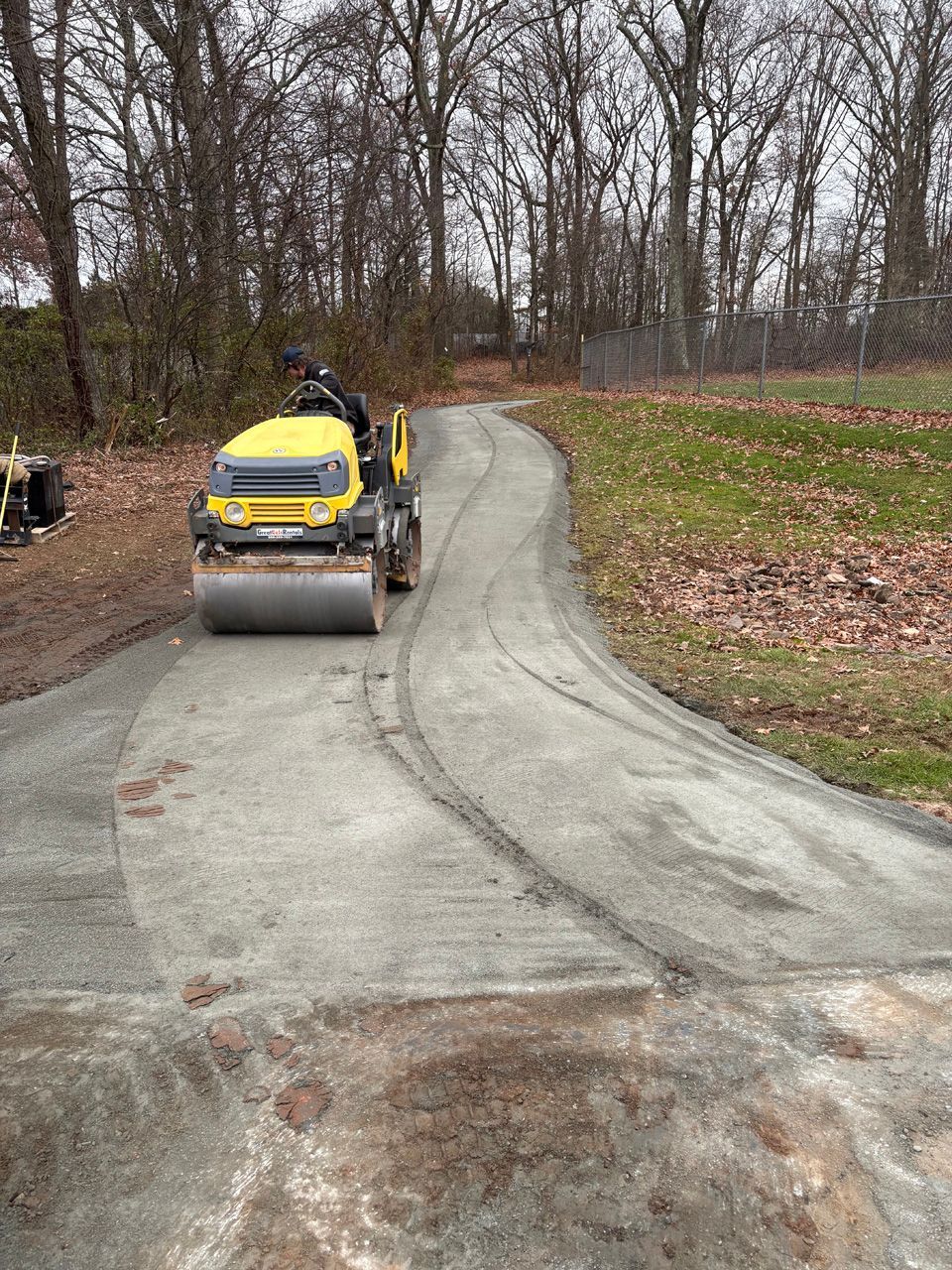 Yellow road roller paving a winding gravel path in a wooded area