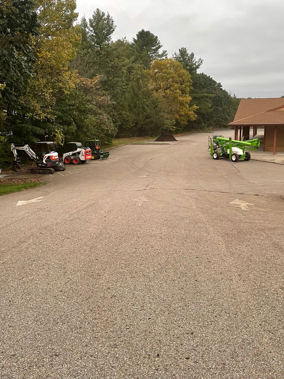 Gravel lot with parked ATVs by trees and a small building on the right.