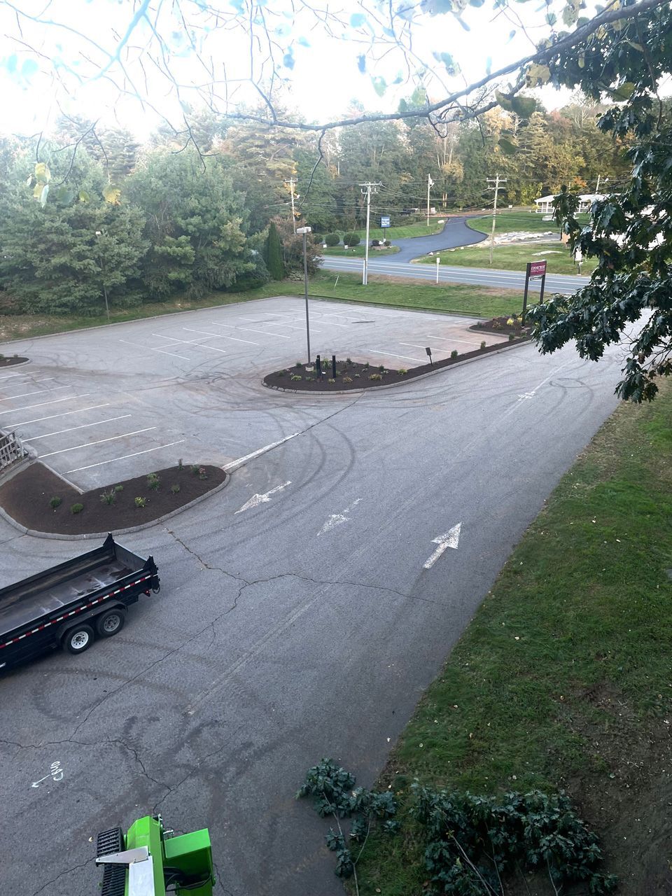 Empty parking lot with a tow truck, small tree island, and roadside greenery in the background