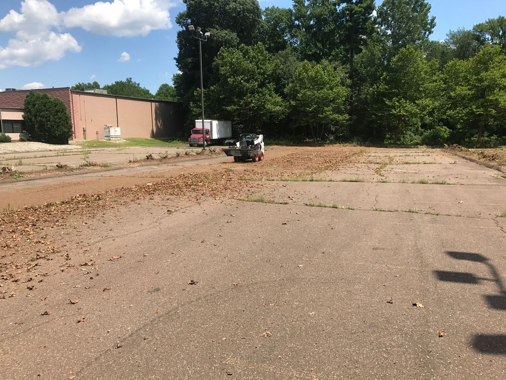 Empty parking lot with a small utility cart and a brown debris pile near trees and a brick building