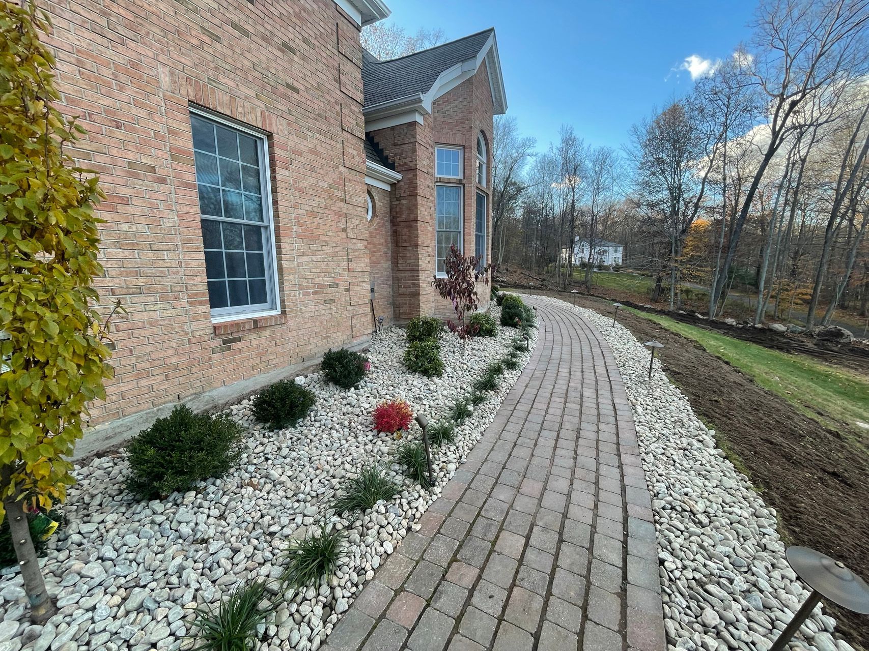 Brick house with white stone landscaping and a curved brick walkway under a clear blue sky