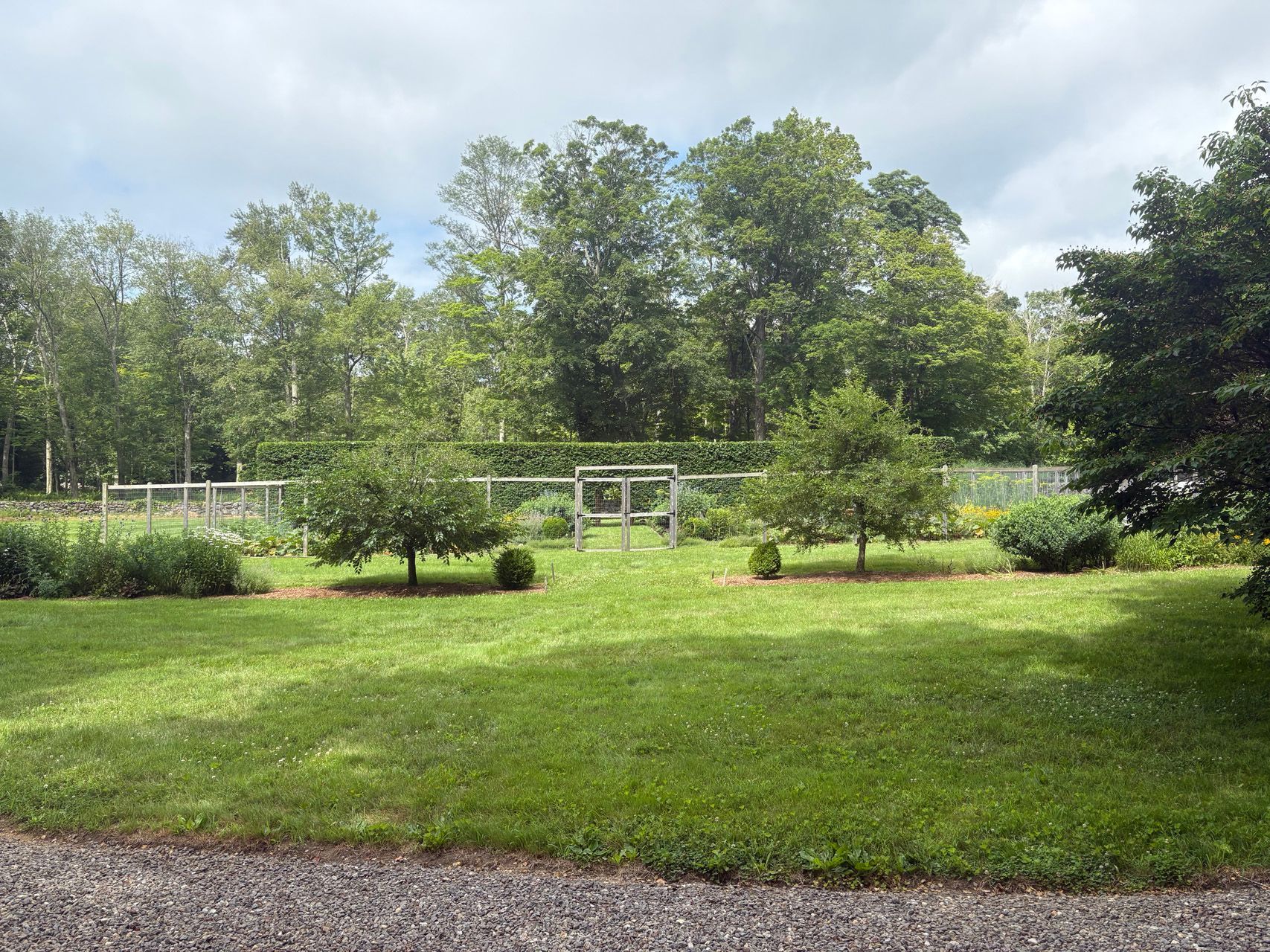 Grassy park with trees, small shrubs, and a gravel path under a partly cloudy sky