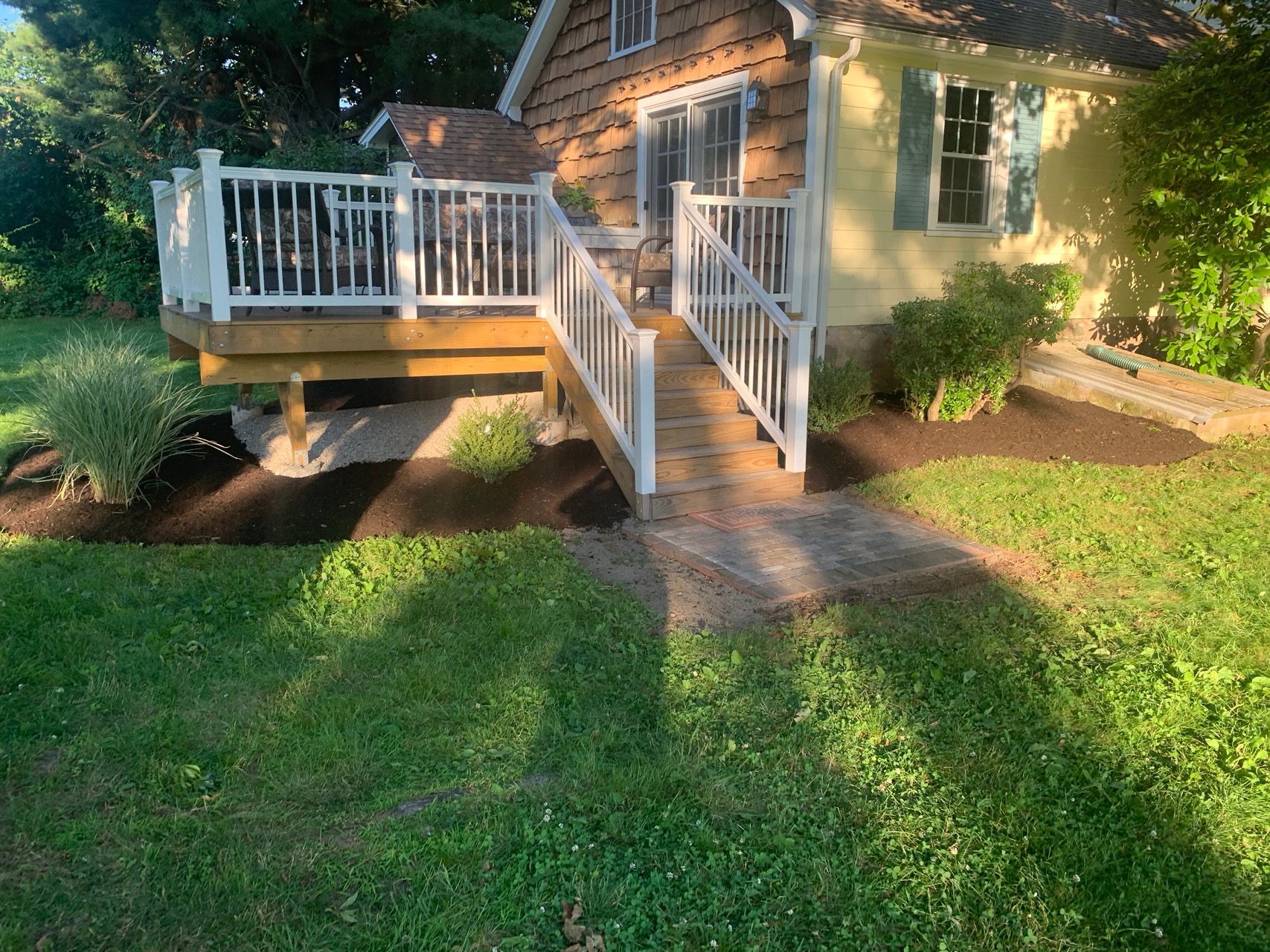 Small cottage with white deck and stairs beside a green lawn in warm evening light