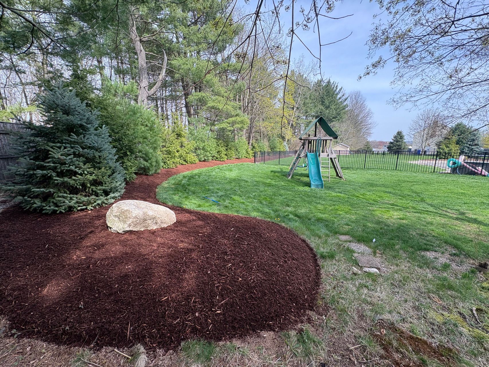 Woodland playground with a dirt mound, red border, and a swing set on a grassy hill