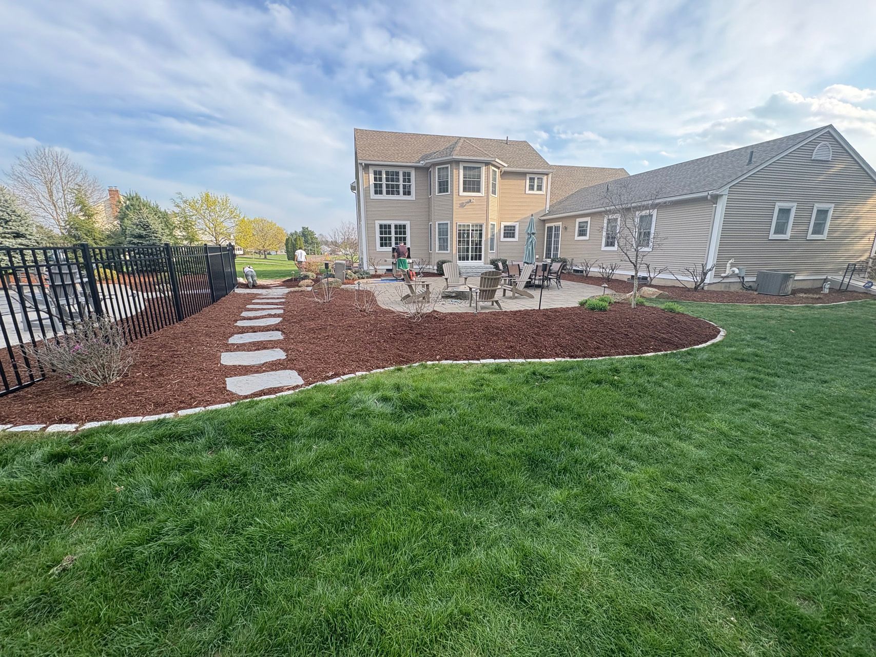 Backyard patio with stone path, green lawn, red mulch, and a two-story house under a cloudy sky