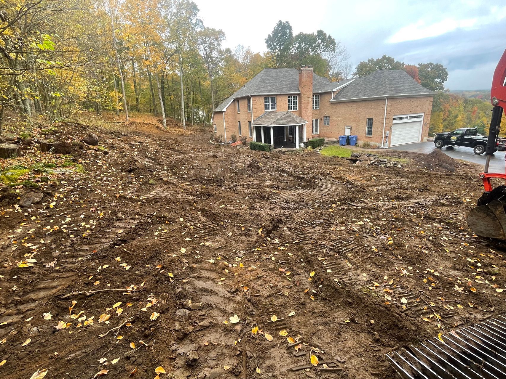 Mud-covered construction site beside a brick house with trees in autumn.