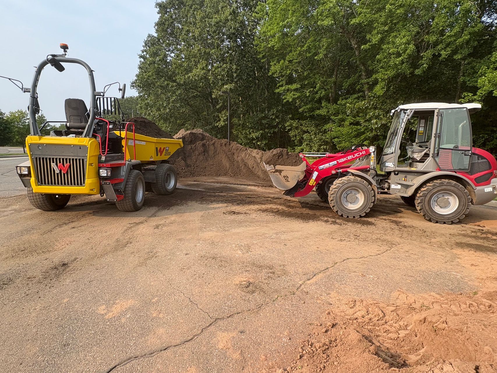Red tractor and yellow dump truck on a dirt road at a wooded construction site