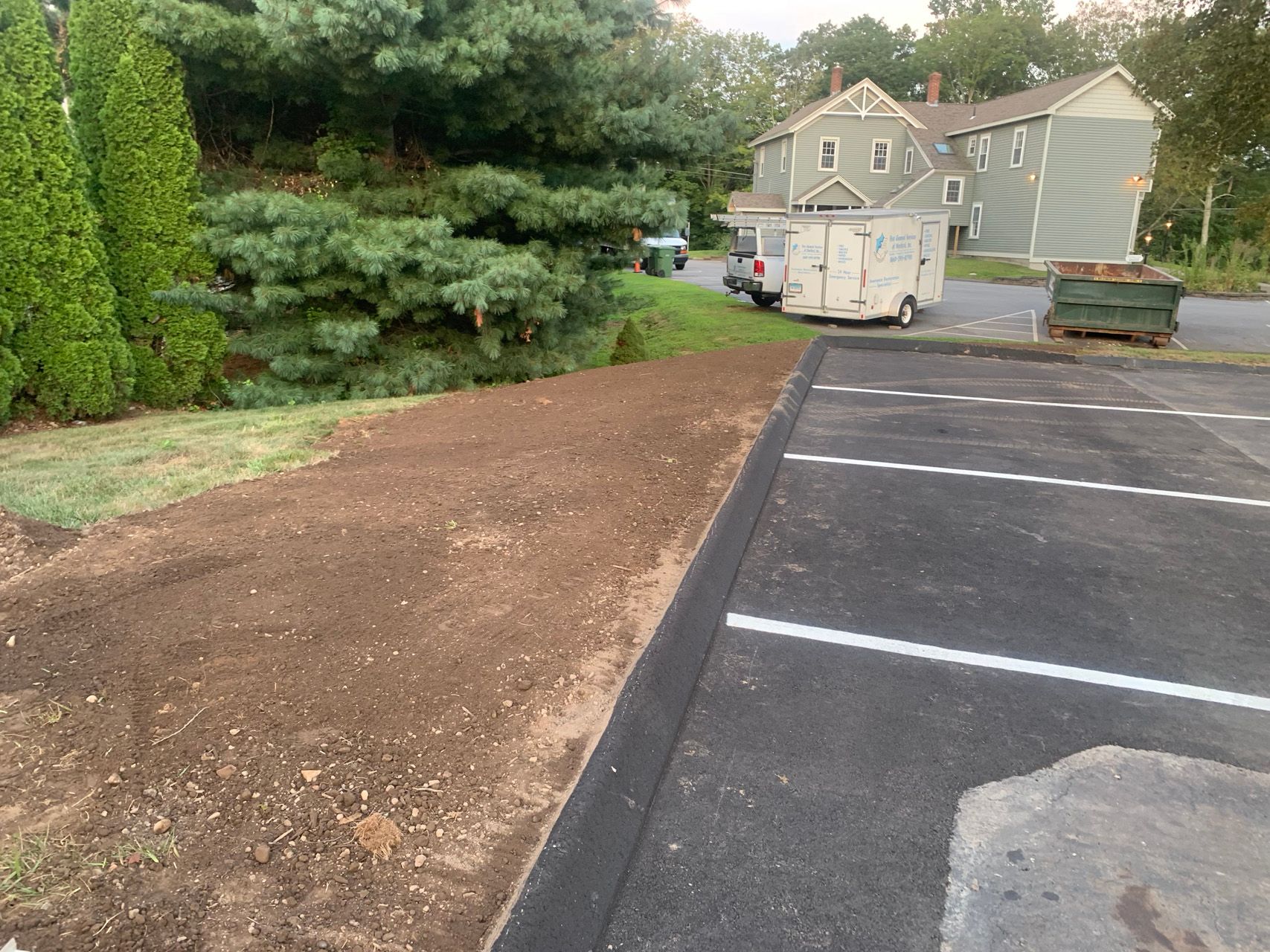 Gravel path beside an apartment parking lot, with trees and a dumpster in the background