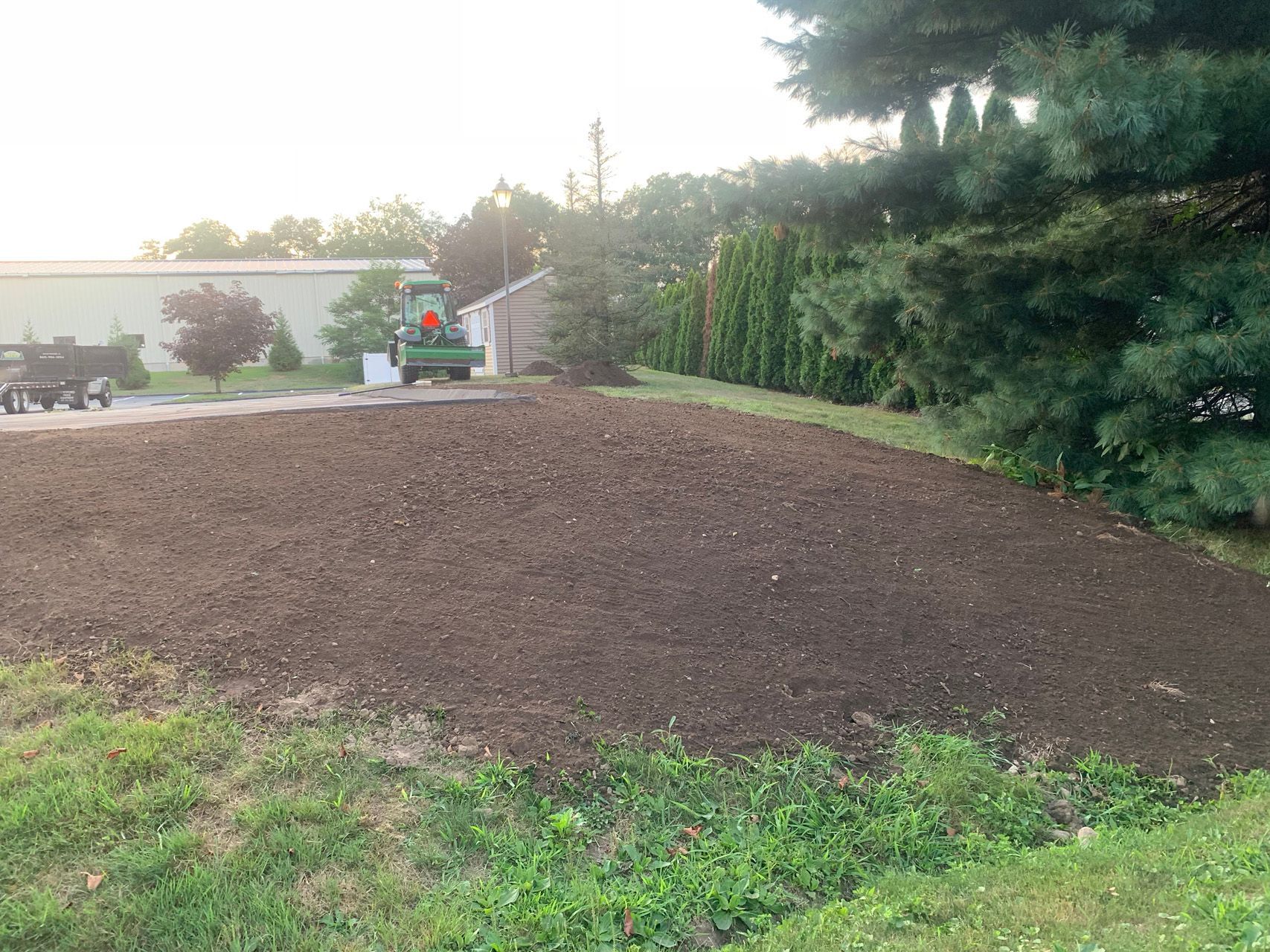 Freshly tilled brown soil on a landscaped yard beside evergreen trees and a small house