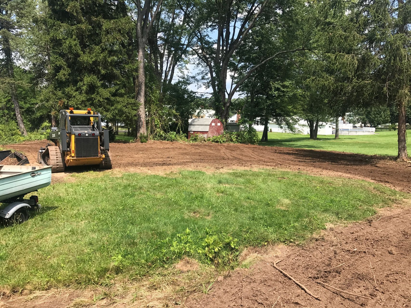 Yellow skid steer grading dirt in a grassy yard with trees in the background