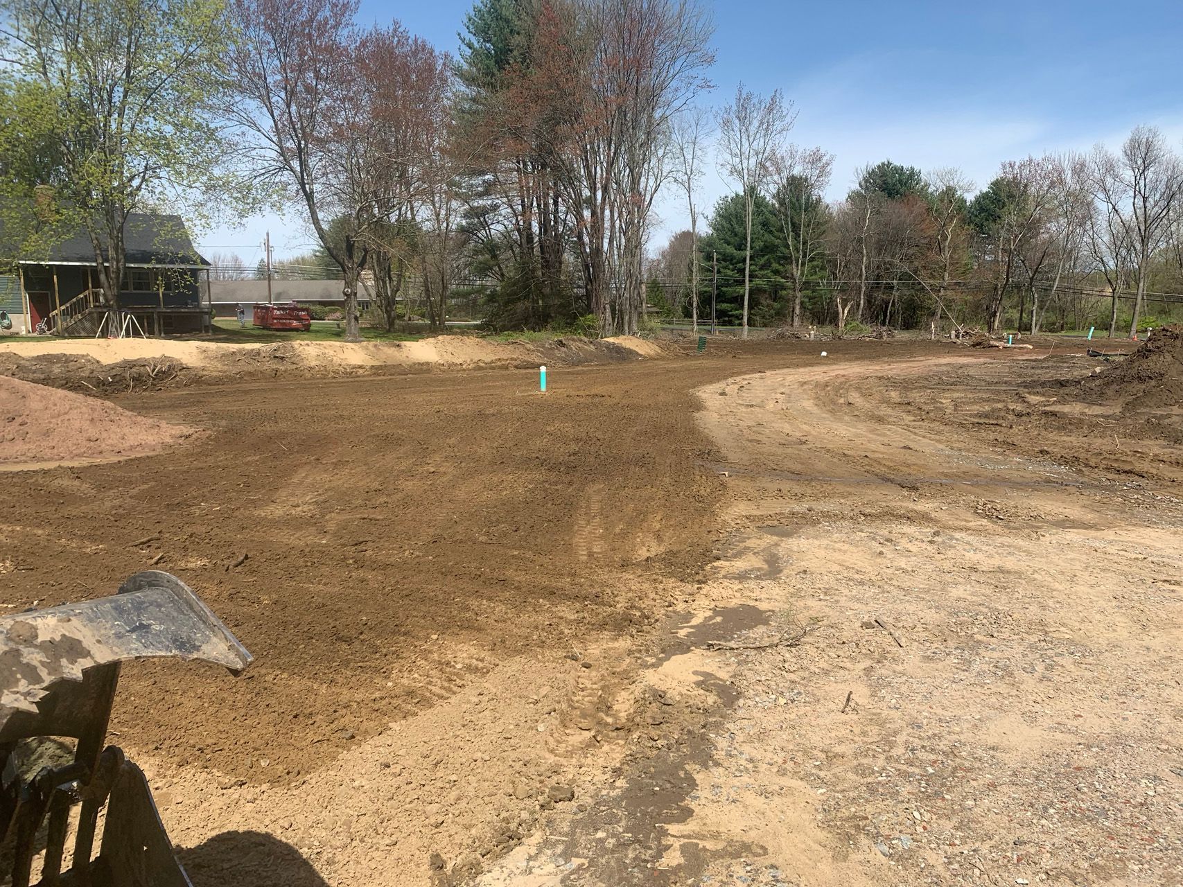 Bare dirt construction site with graded earth, trees in the background, and a clear blue sky