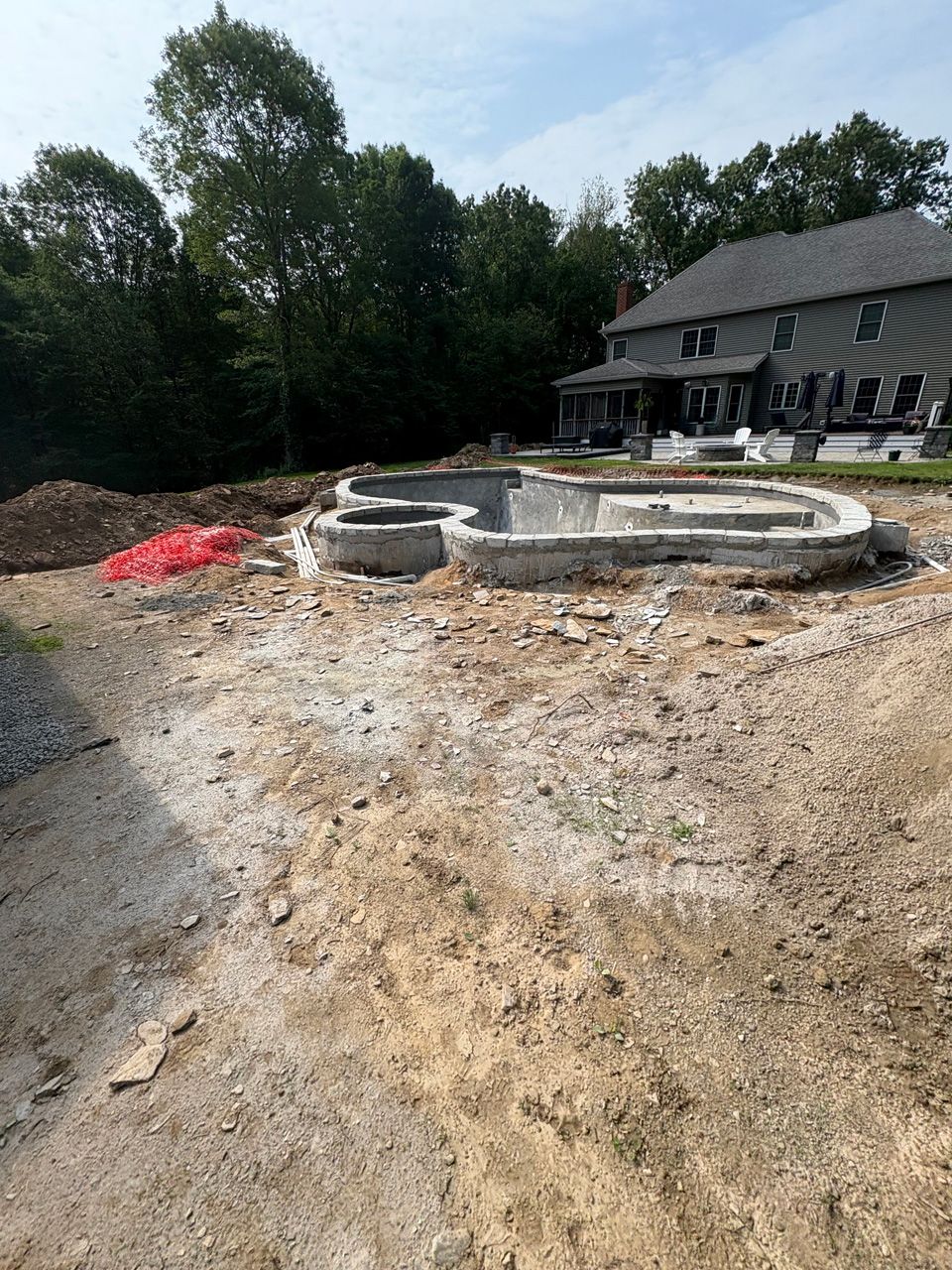 Backyard construction site with a circular stone patio and fire pit beside a house