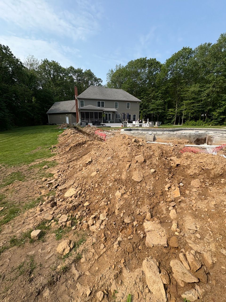 Backyard construction site with dirt mound, unfinished patio, and a house in the background