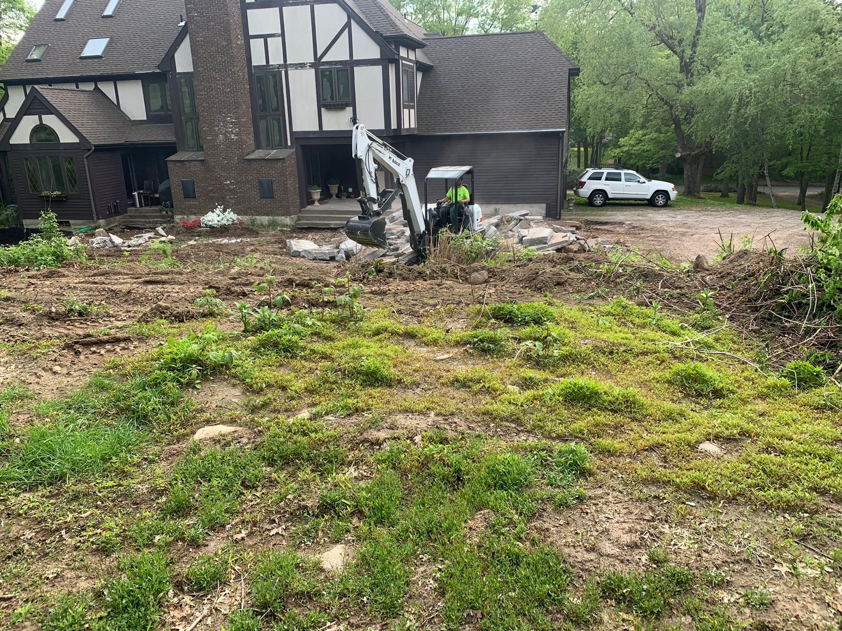 Half-timbered house with a damaged front yard, debris, and a white SUV parked nearby under overcast skies