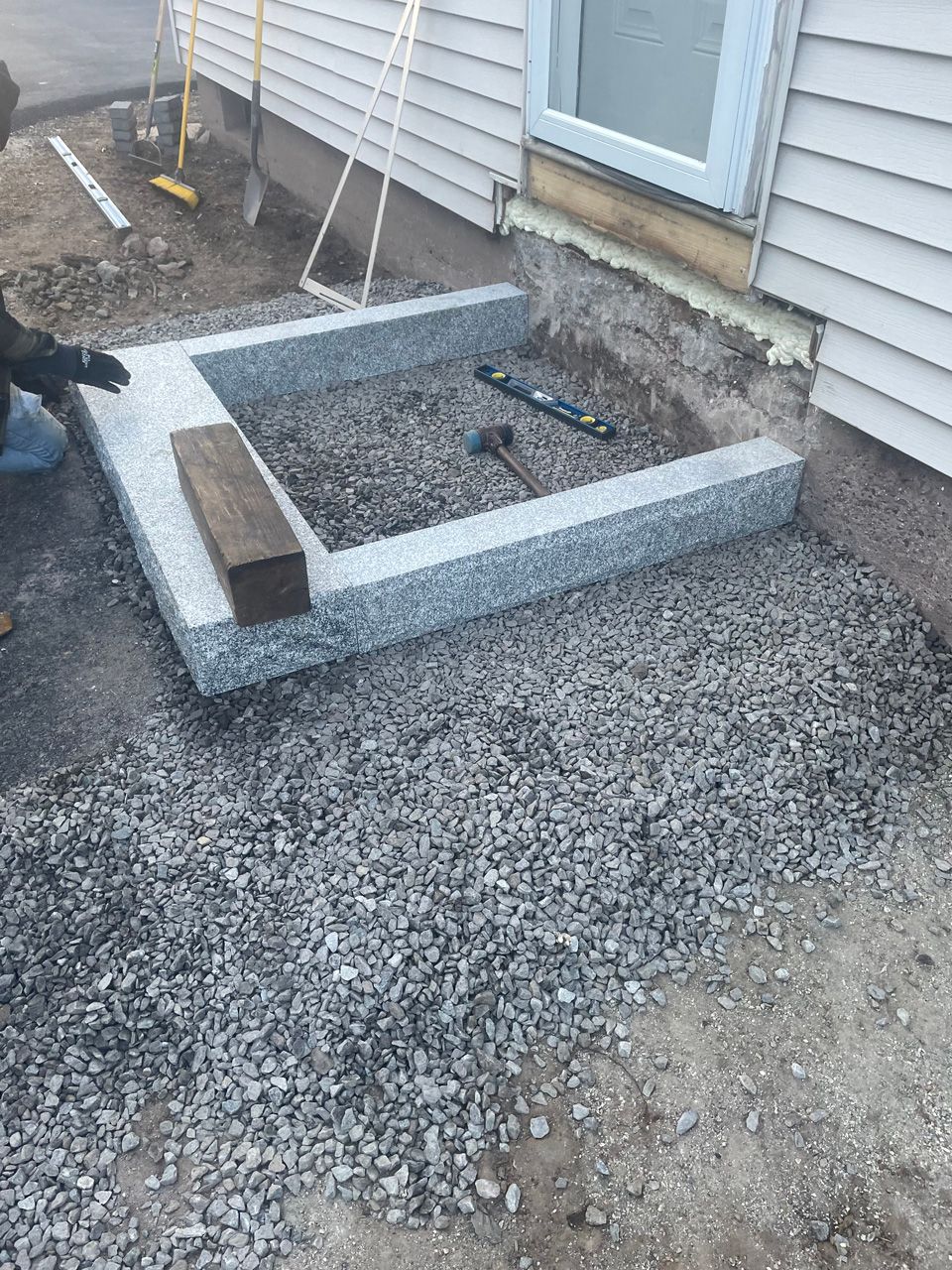 Concrete planter bed under construction beside a house, with gravel, soil, and tools nearby.