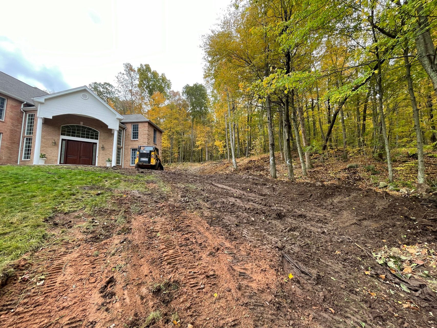 Newly cleared dirt lot beside a house, bordered by autumn trees with yellow leaves.