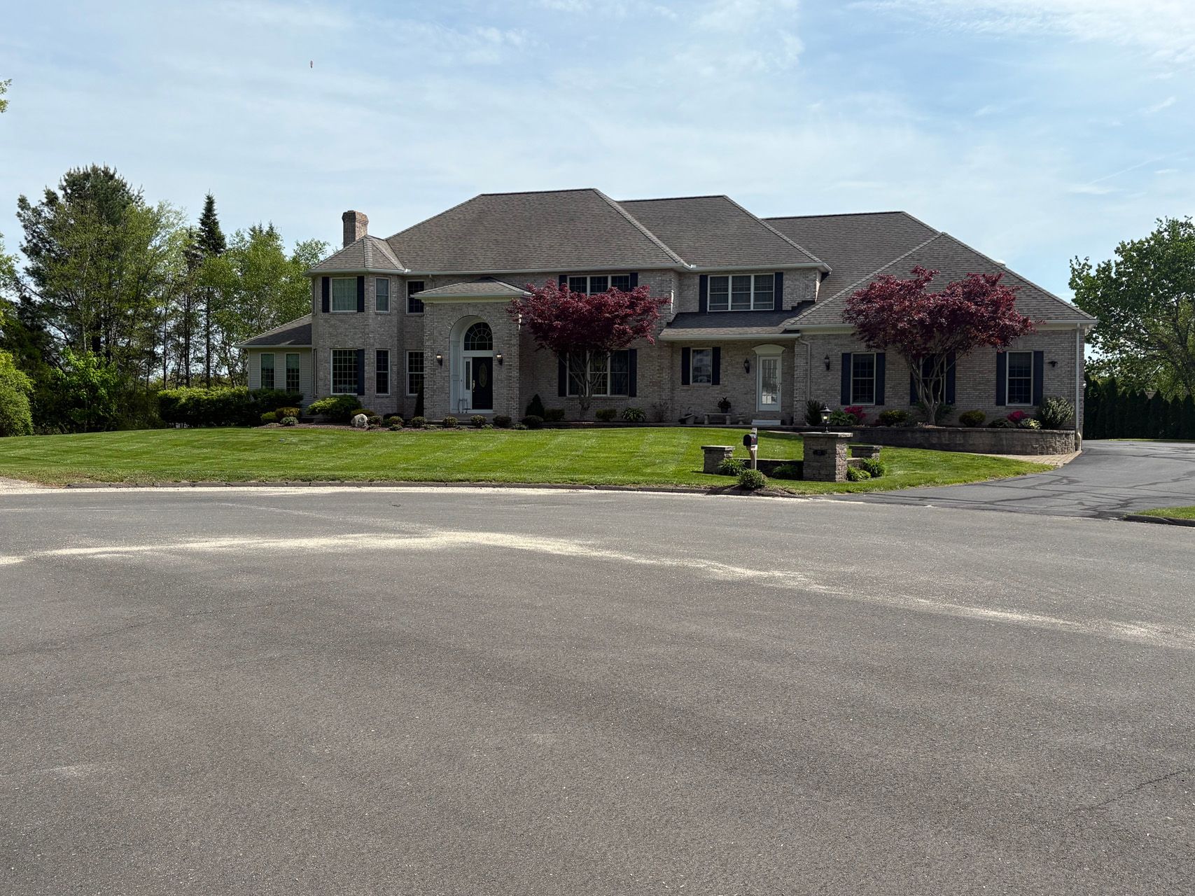 Large stone house with red trees in front, viewed across an empty paved lot
