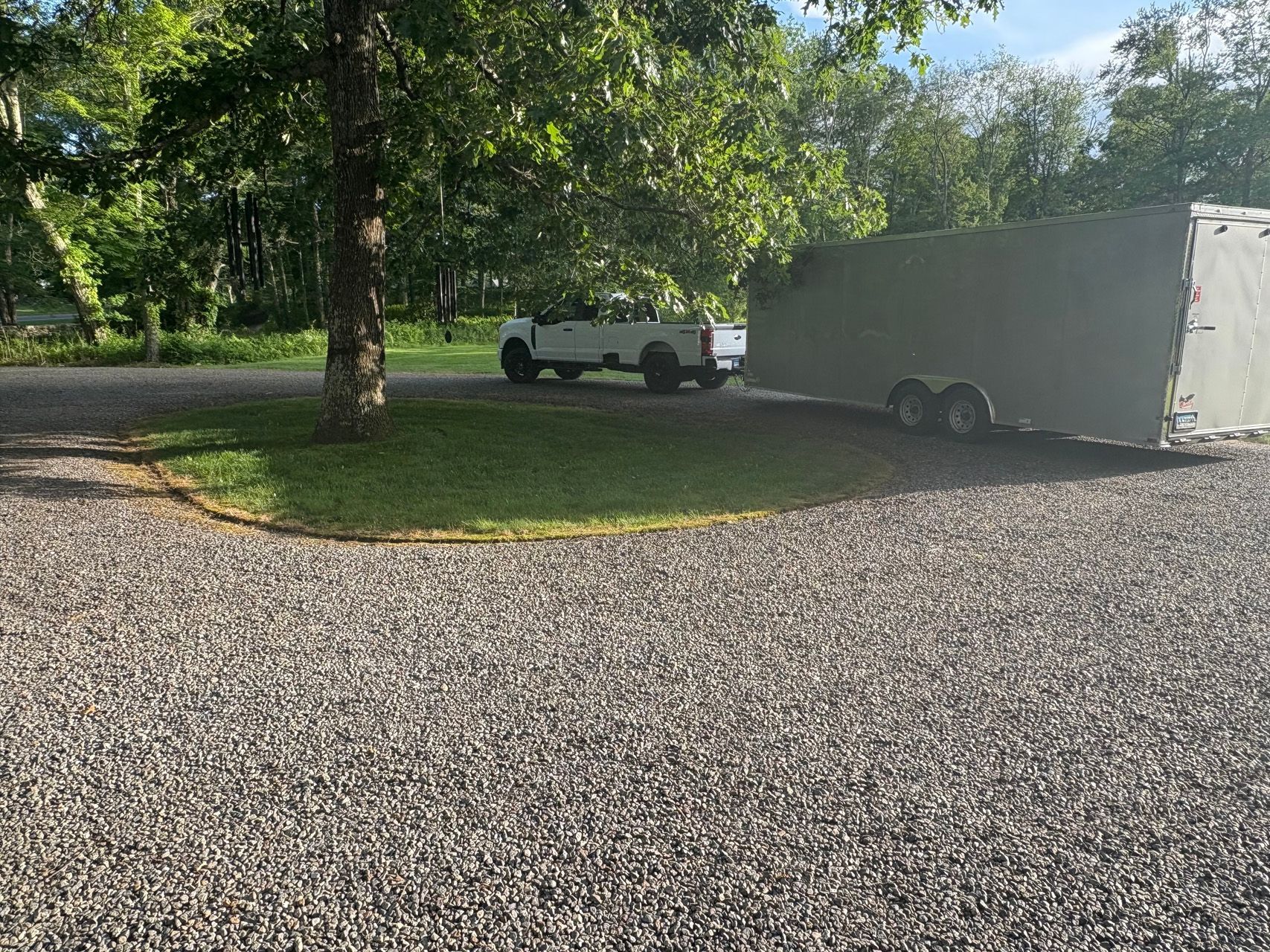 White truck with enclosed trailer parked on a gravel driveway under trees.