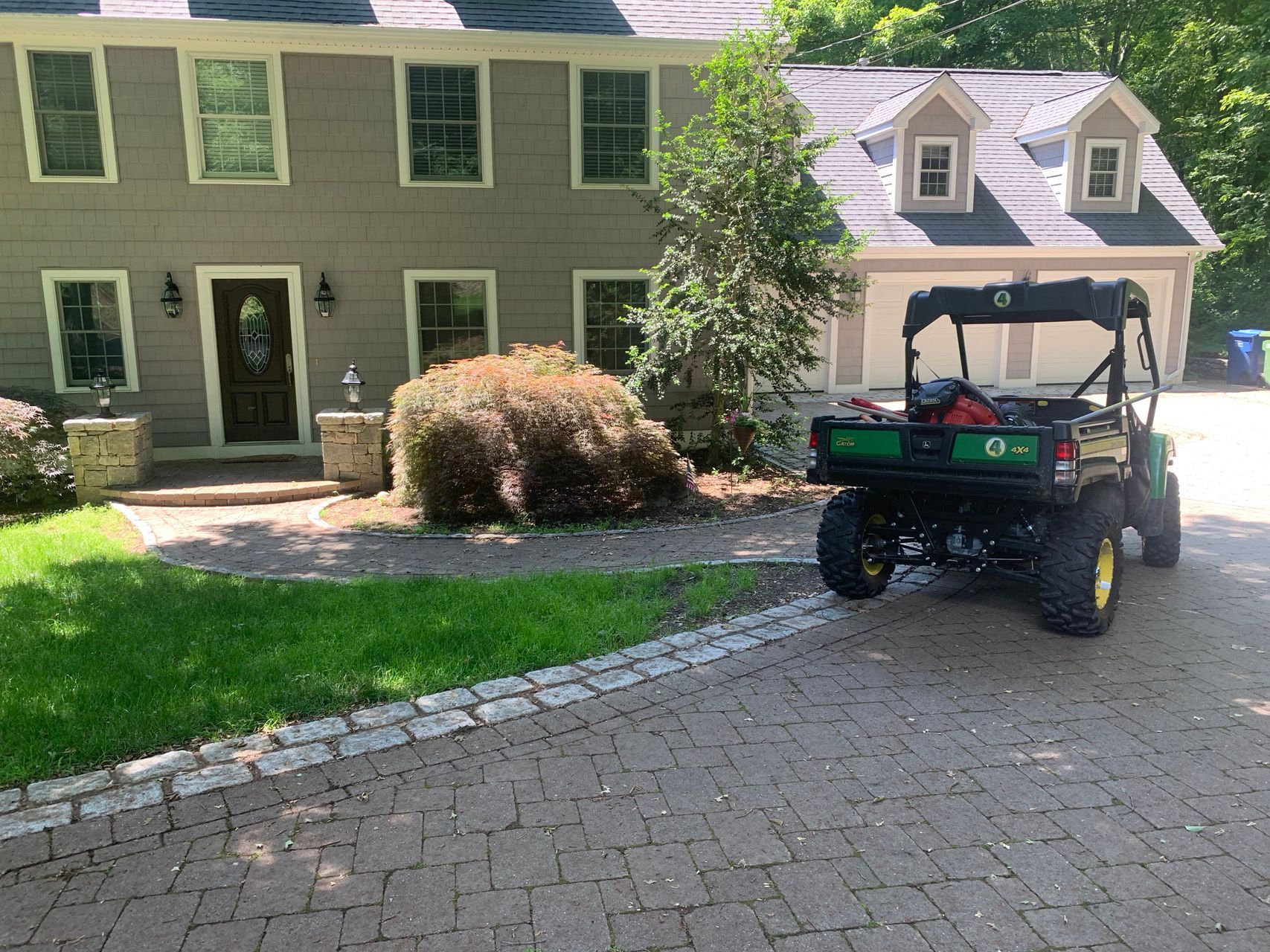 Green house with a paved driveway and a utility cart parked near the garage.