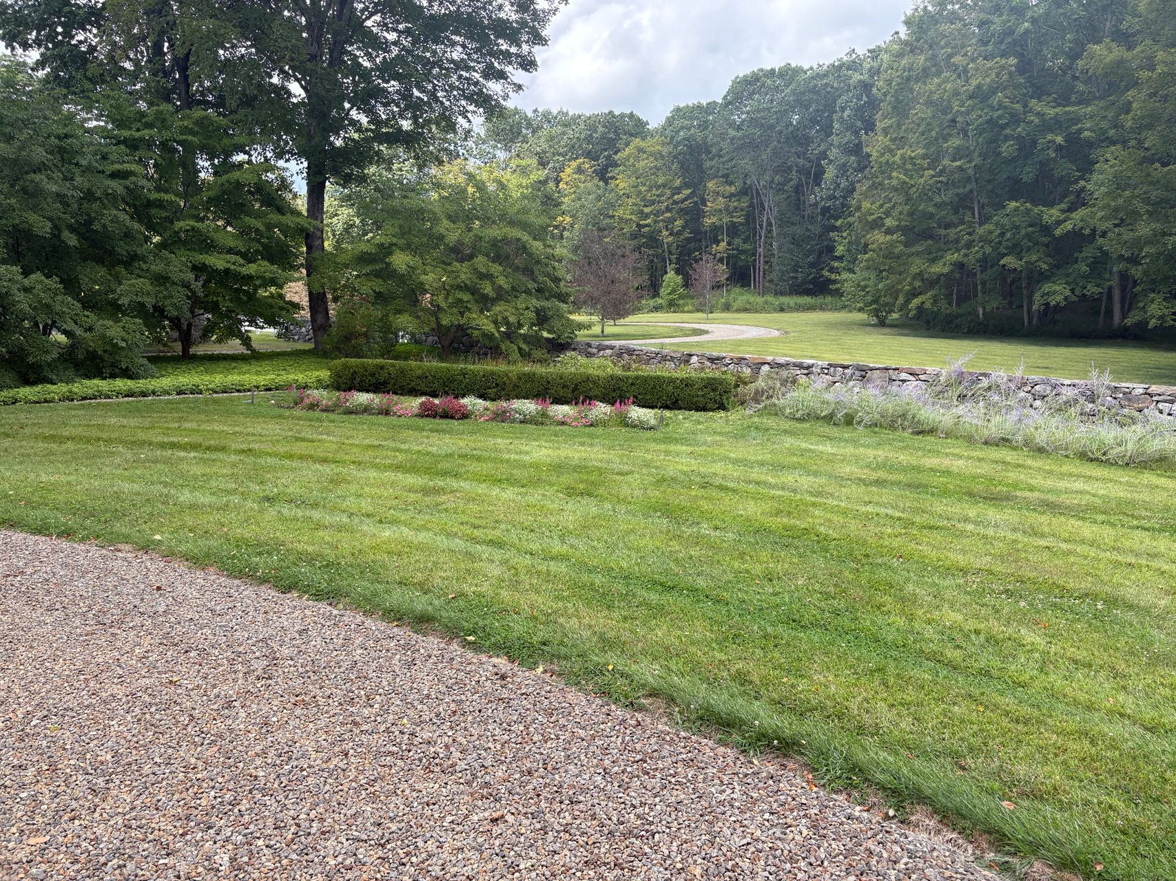 Gravel path beside a manicured lawn, flower bed, and trees in a quiet park