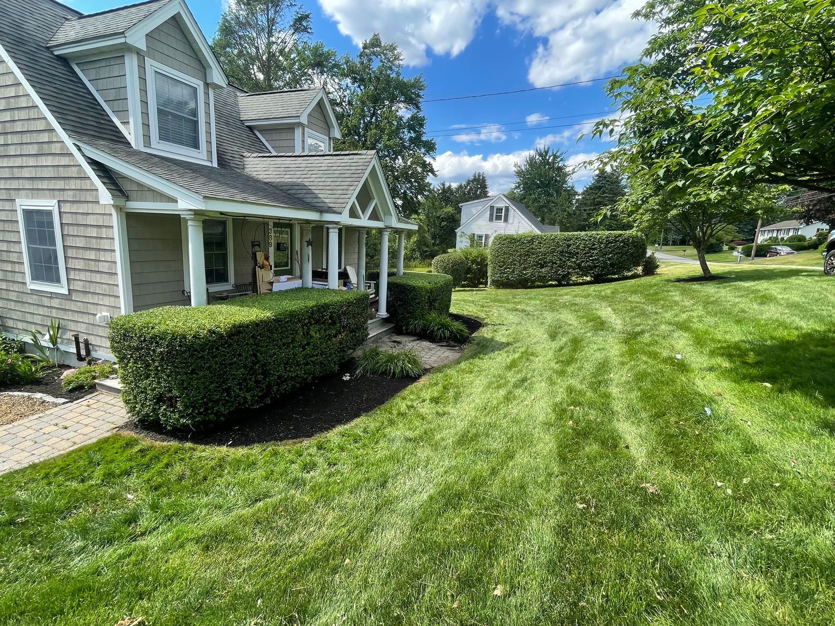 Suburban home with a porch, manicured lawn, and blue sky on a sunny day