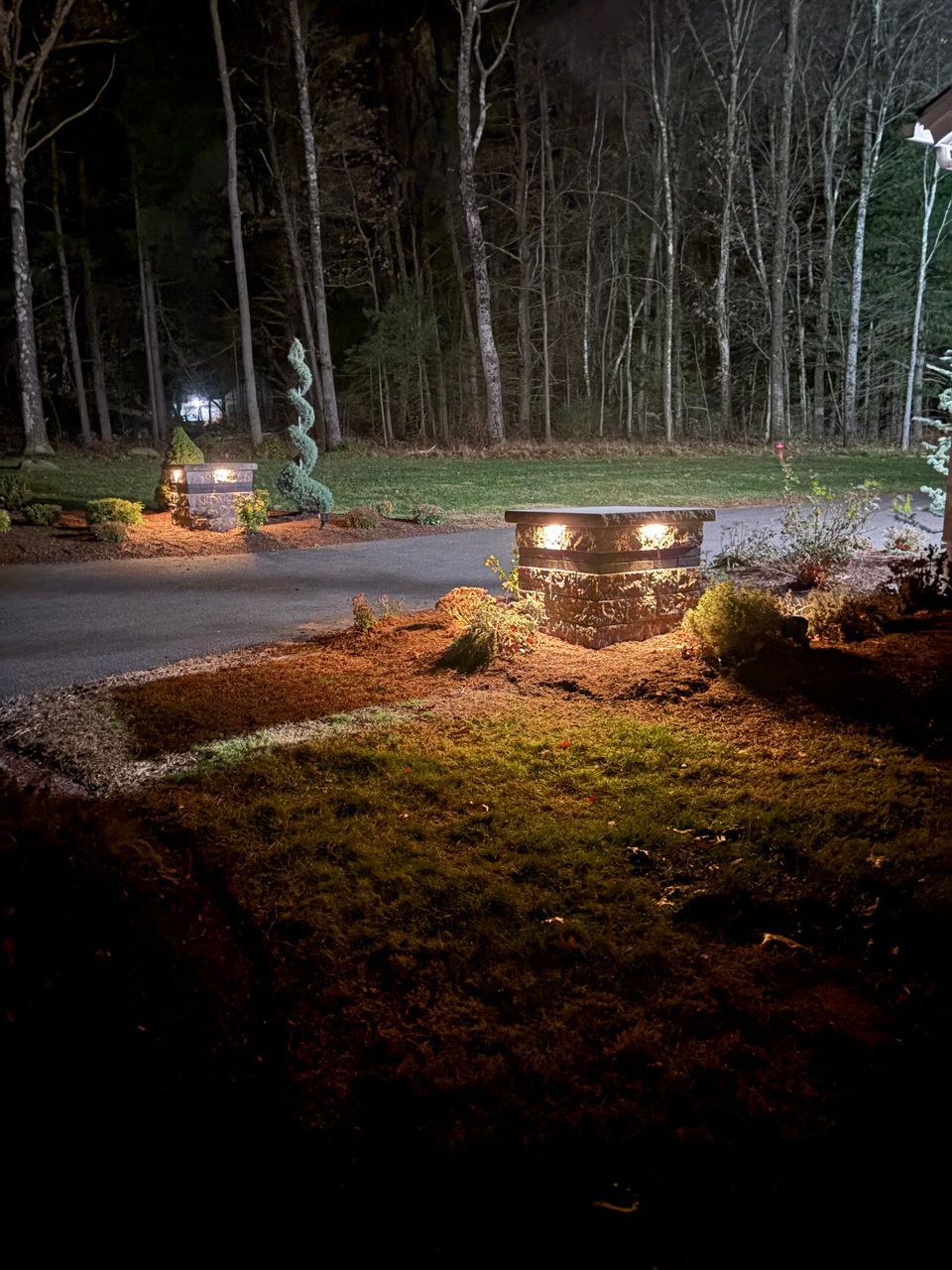Lit stone garden lights illuminate a path at night beside bare trees and grass.